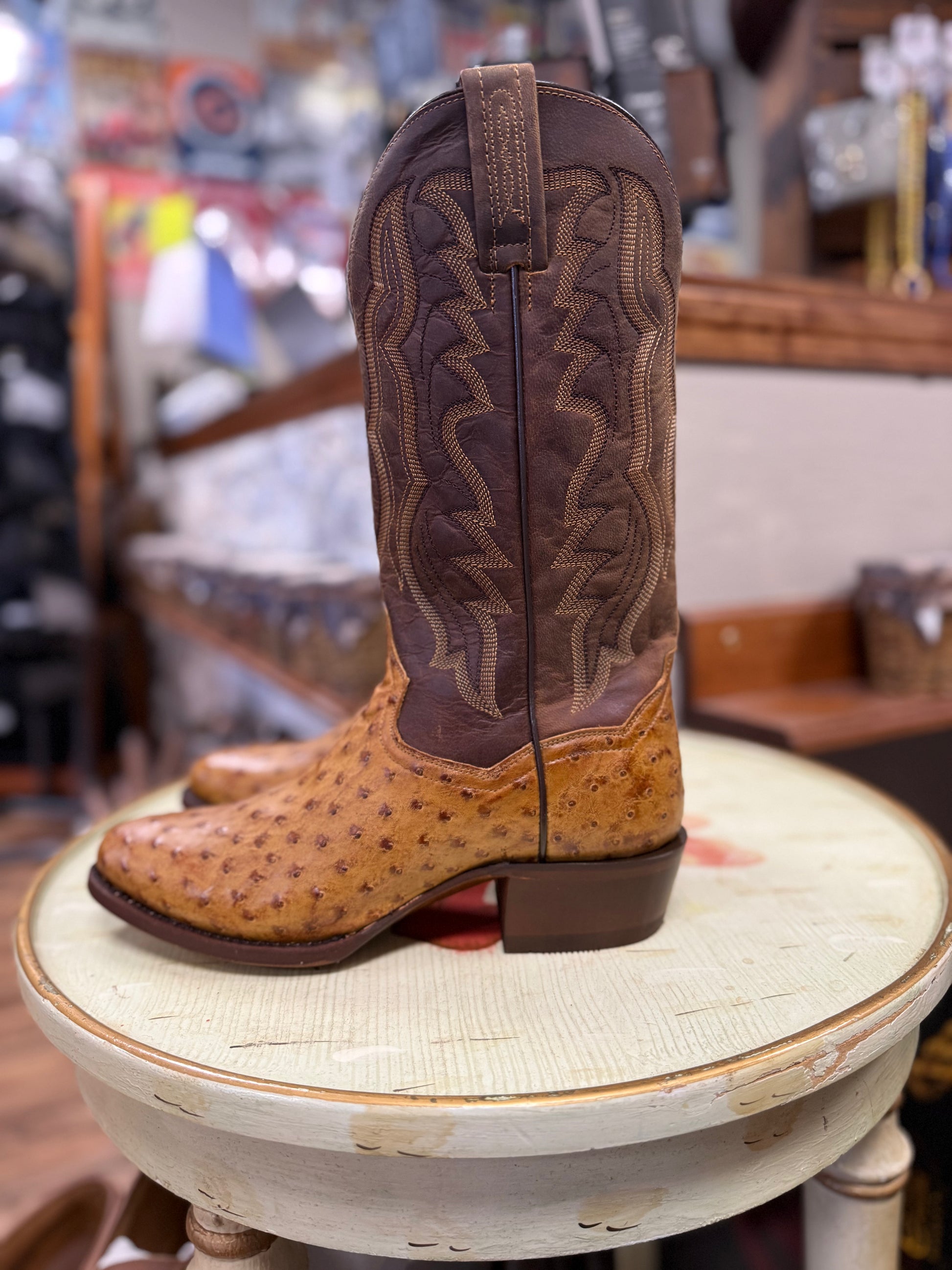 Brown and tan cowboy boot on a round white surface with a blurred store background
