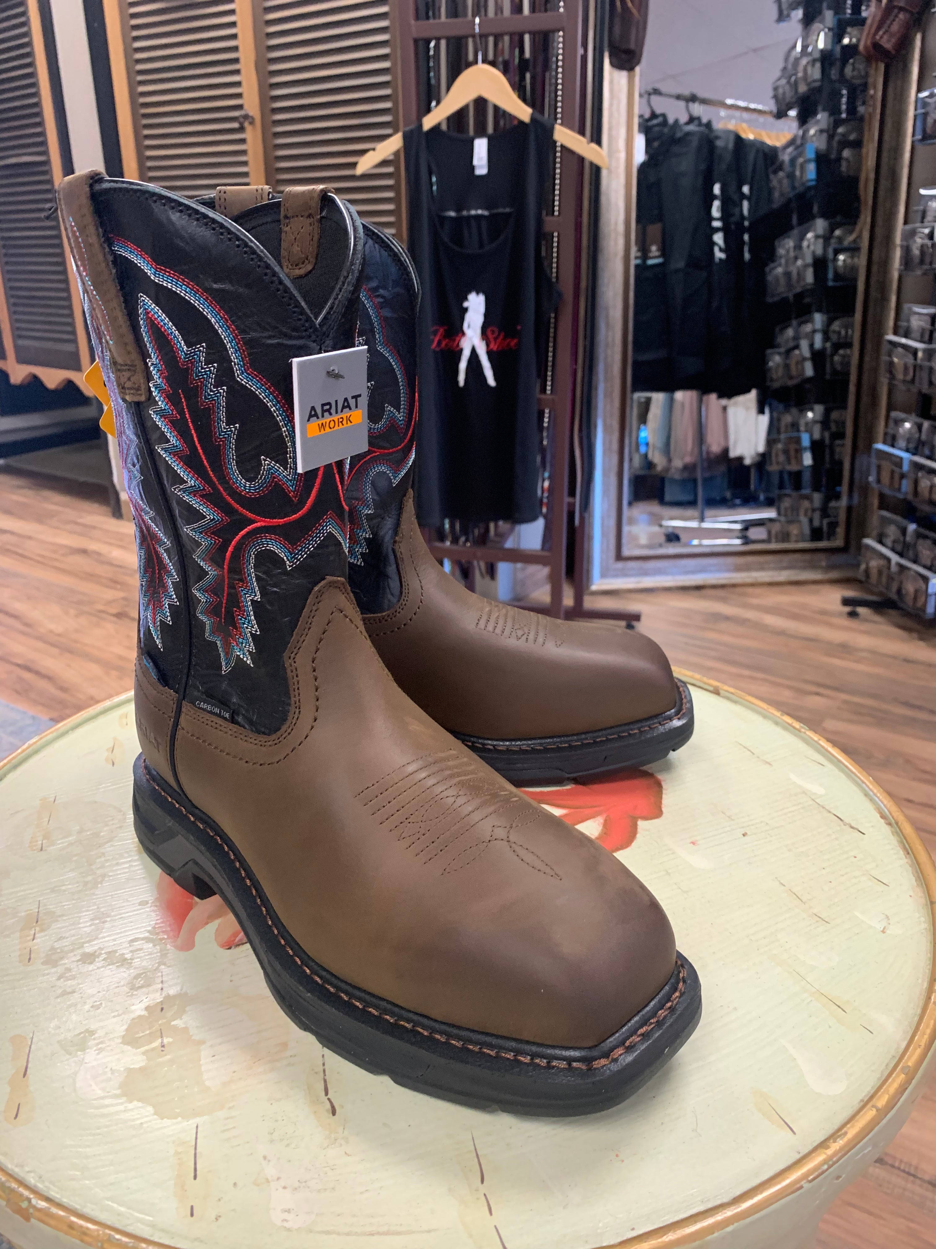 A pair of brown, waterproof work boots with a carbon toe and a low heel, displayed on a wooden platform inside a retail store.