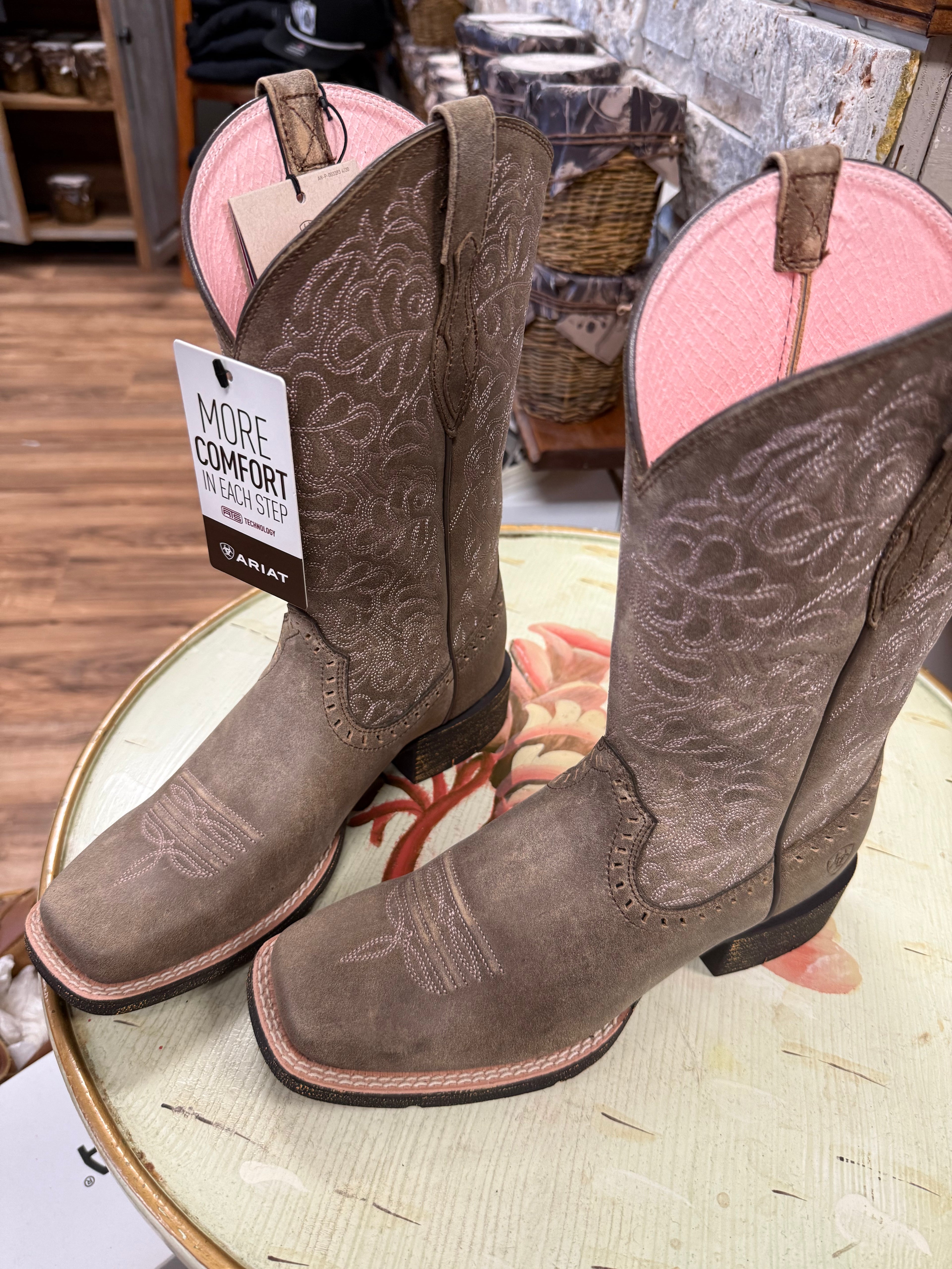 Pair of brown Ariat boots on a round surface with a store interior background.