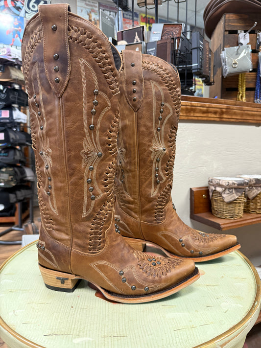 Pair of brown cowboy boots with intricate designs on a round surface in a store setting.