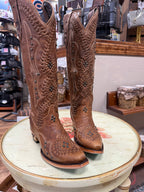 Pair of brown cowboy boots with intricate designs on a round table in a store setting.
