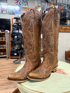 Pair of brown cowboy boots with intricate designs on a table in a store setting.