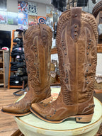 Pair of brown cowboy boots with intricate designs on a round surface, with a store interior in the background.