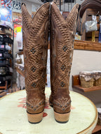 Pair of brown cowboy boots with intricate designs on a round surface in a store setting.