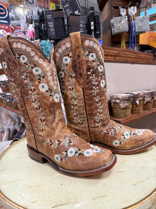Pair of brown embroidered cowboy boots on a wooden surface with a store background.