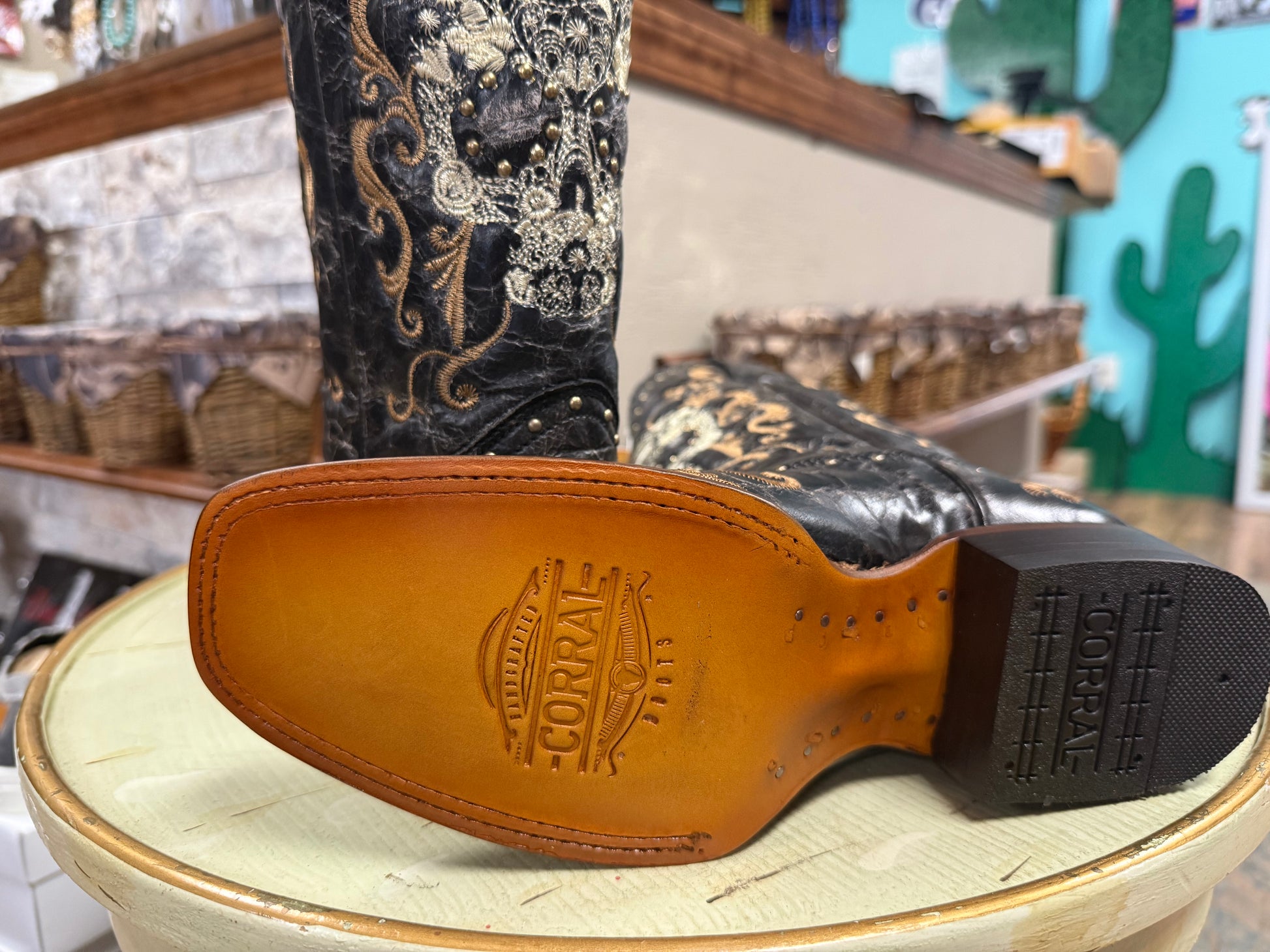 Close-up of a black cowboy boot with intricate patterns on a wooden stool in a store setting.