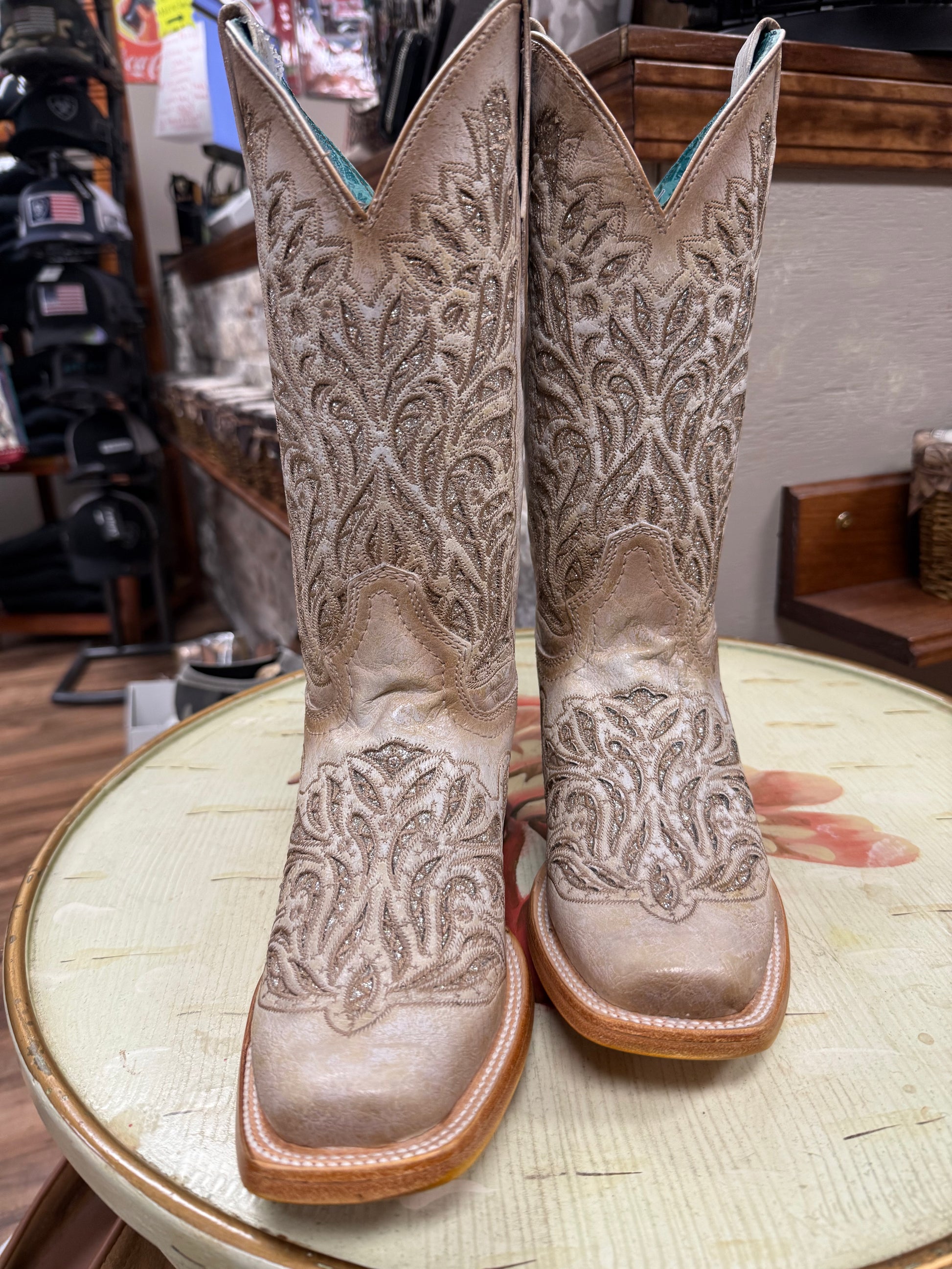 Pair of embroidered cowboy boots on a round table in a store setting.