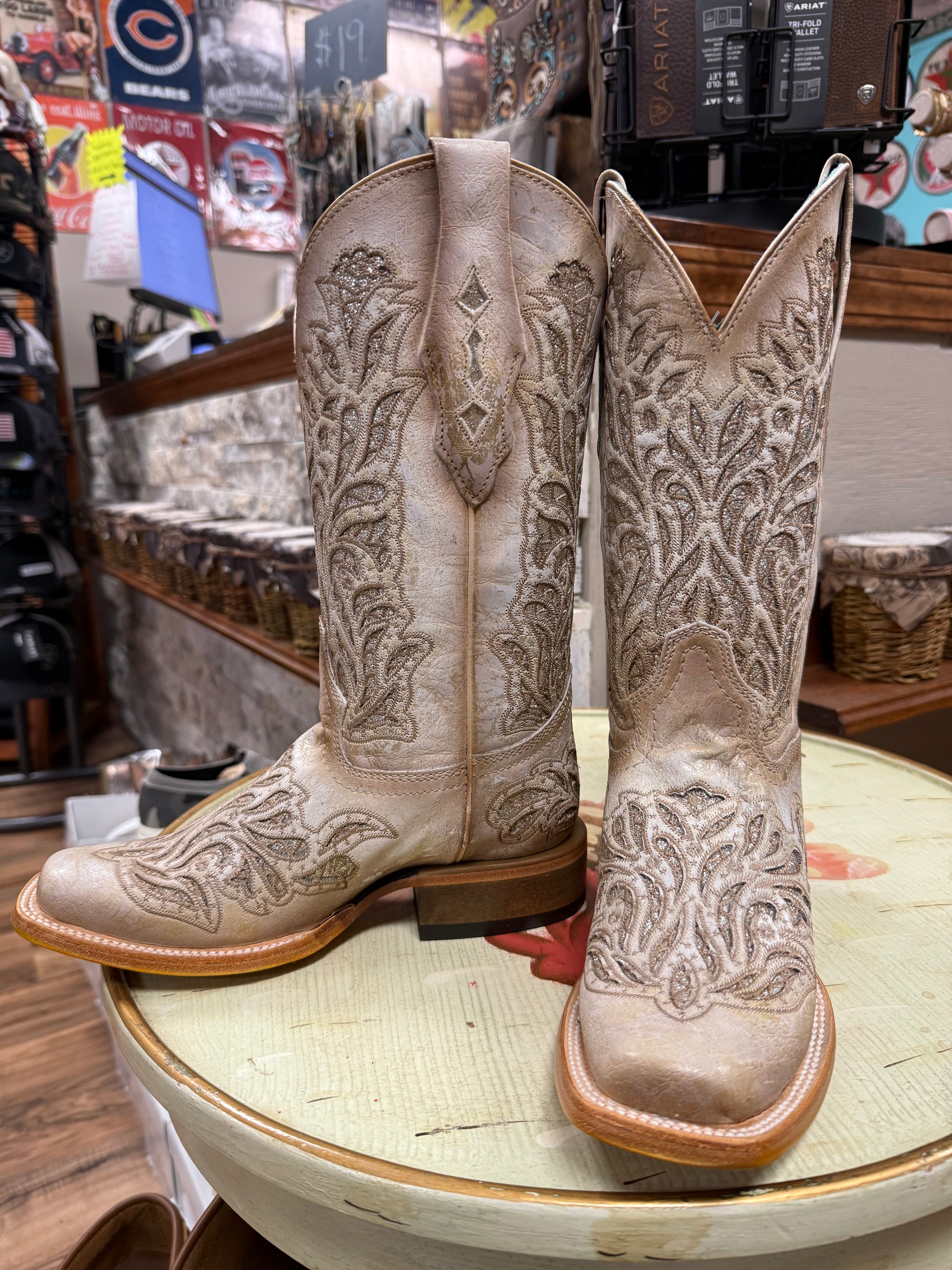 Pair of beige embroidered cowboy boots on a round table in a store setting.