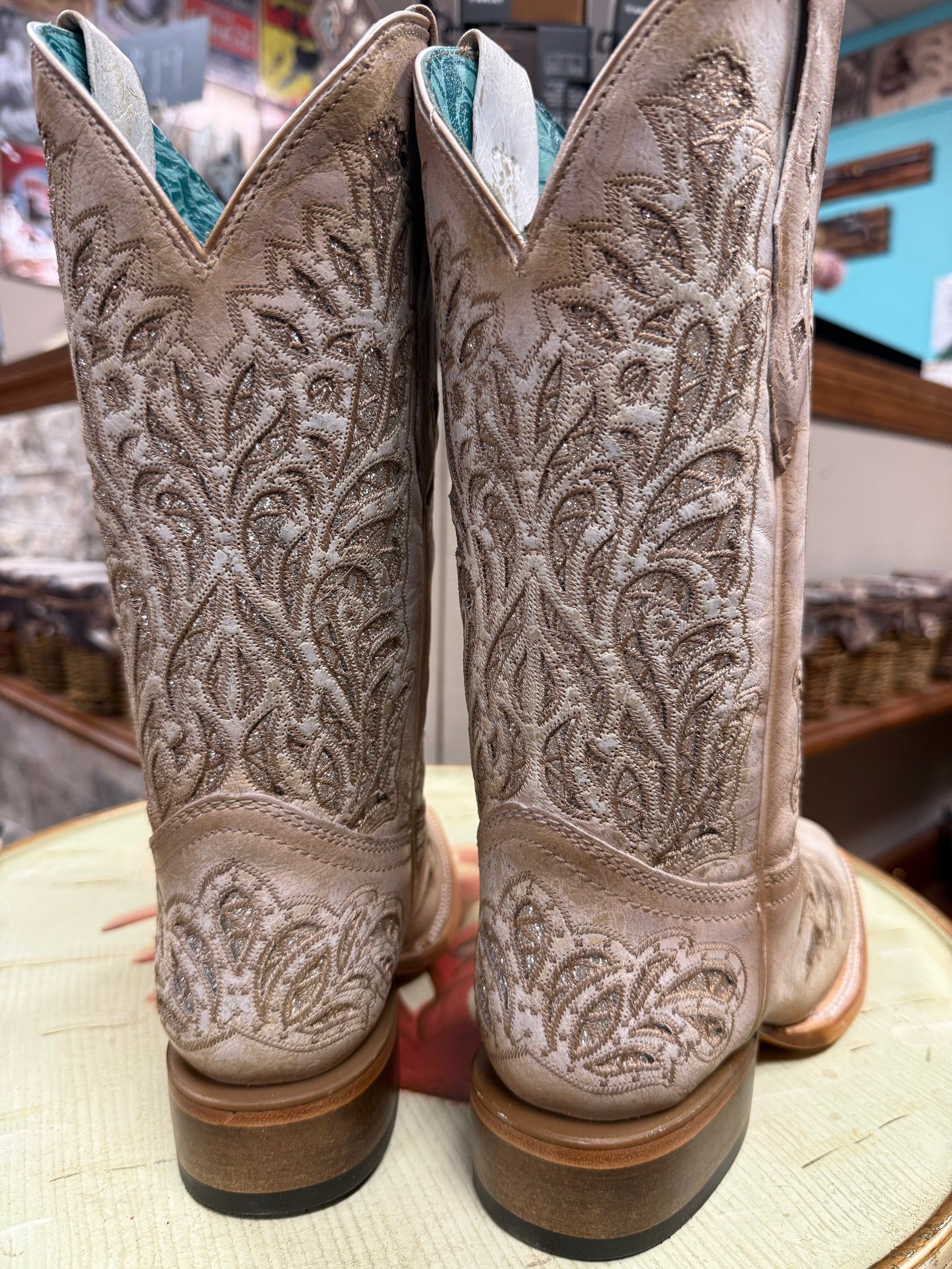 Pair of beige cowboy boots with intricate patterns on a wooden surface.