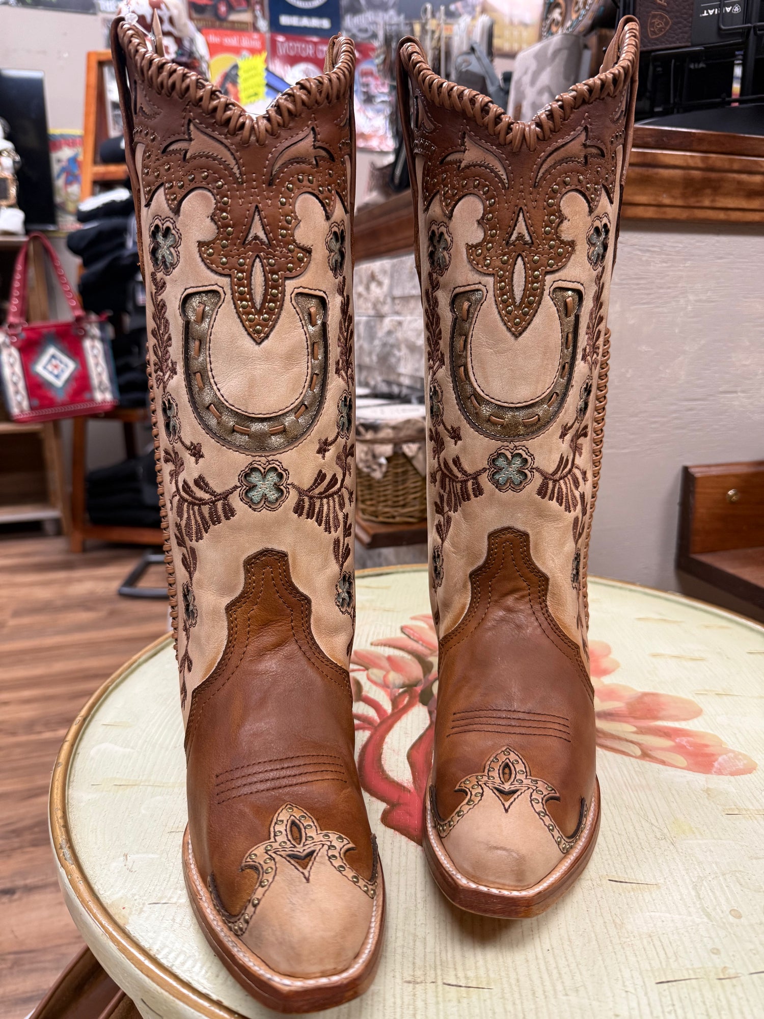 Pair of brown cowboy boots with intricate designs on a round table.
