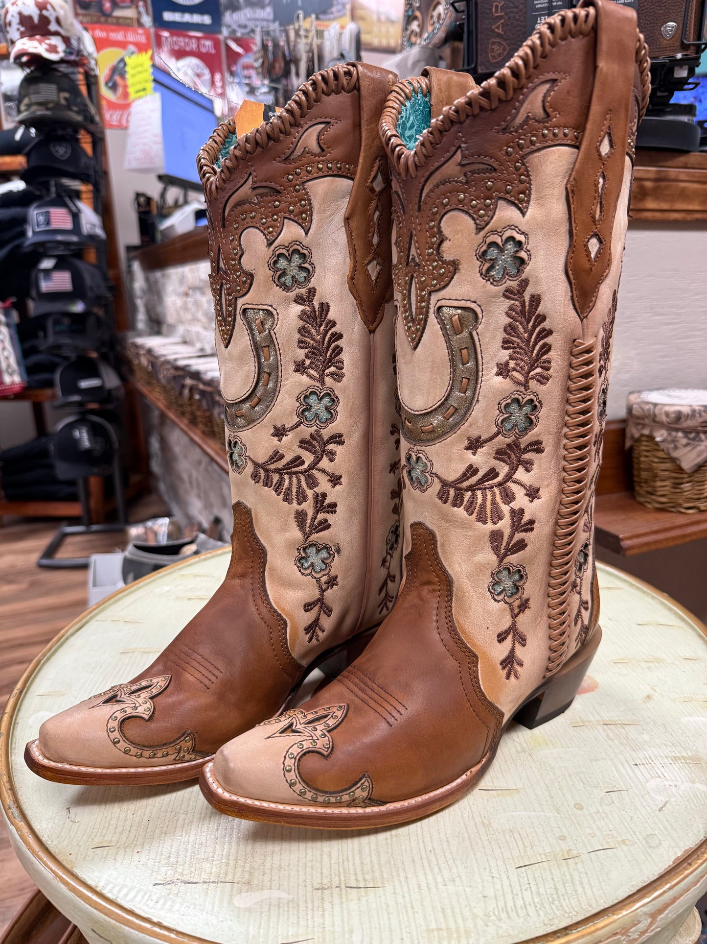 Pair of brown cowboy boots with intricate designs on a round table.