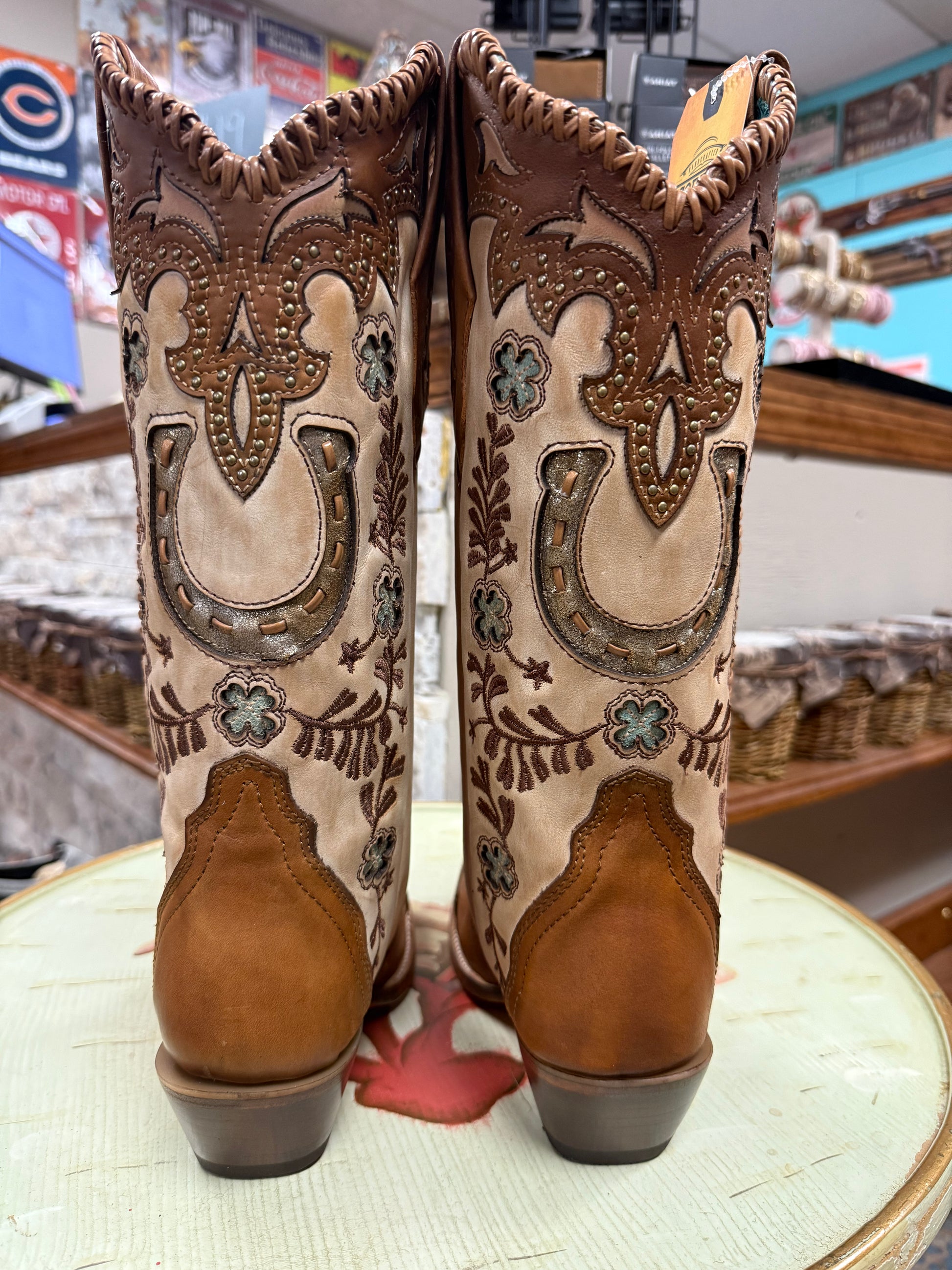 Pair of brown and beige cowboy boots with intricate designs on a round surface.