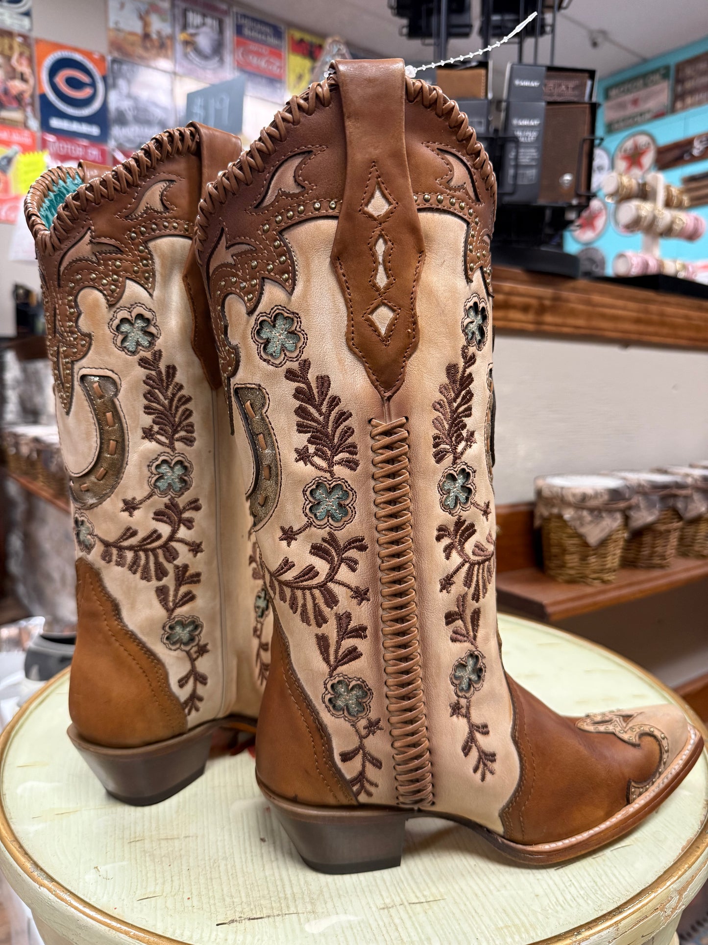 Pair of brown and beige embroidered cowboy boots on a round surface with a store interior background.
