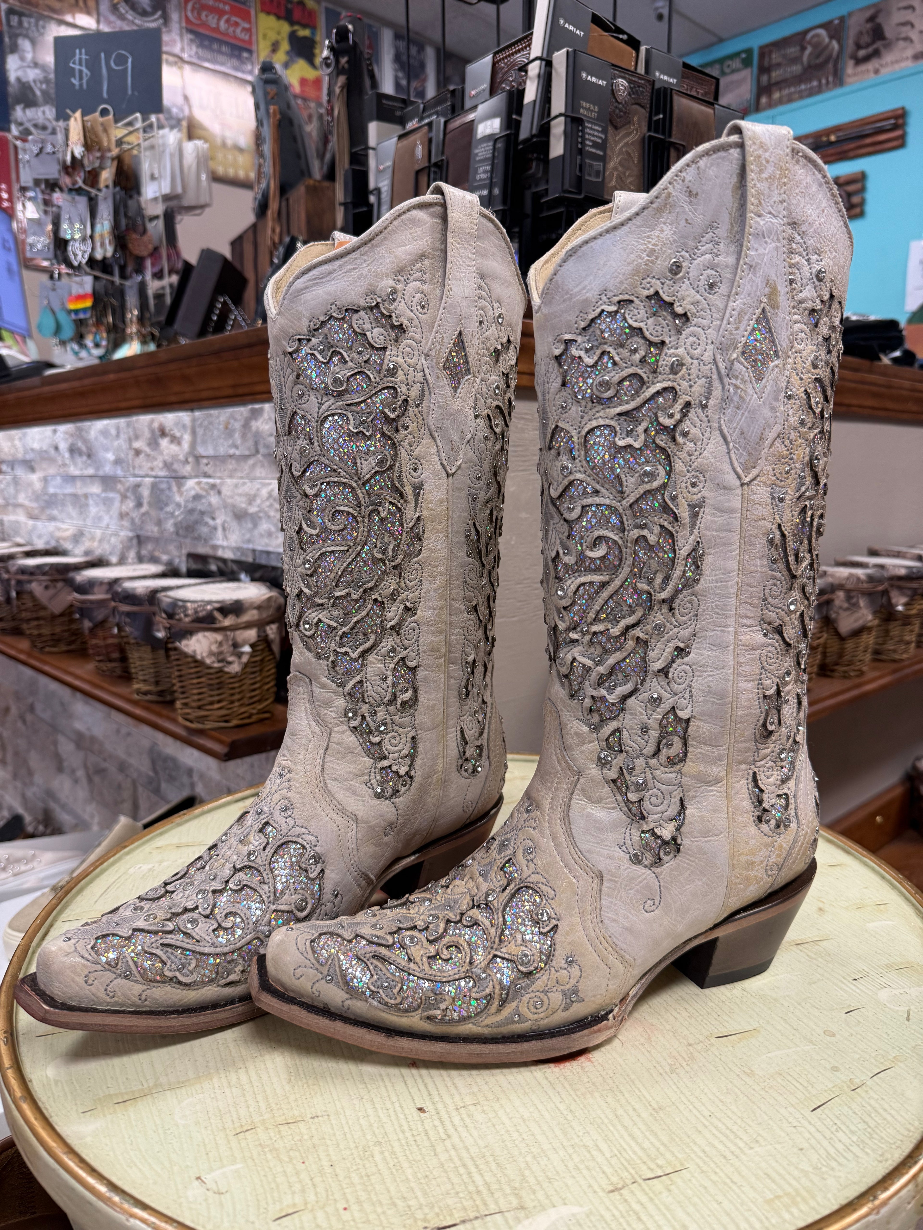 Pair of ornate beige cowboy boots on a round surface with a store interior background.