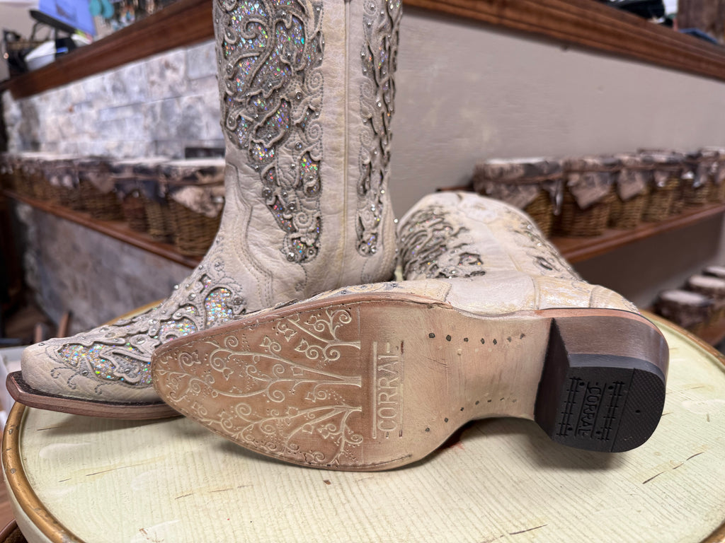 Close-up of white embroidered boots with 'Corral' branding on a wooden surface.