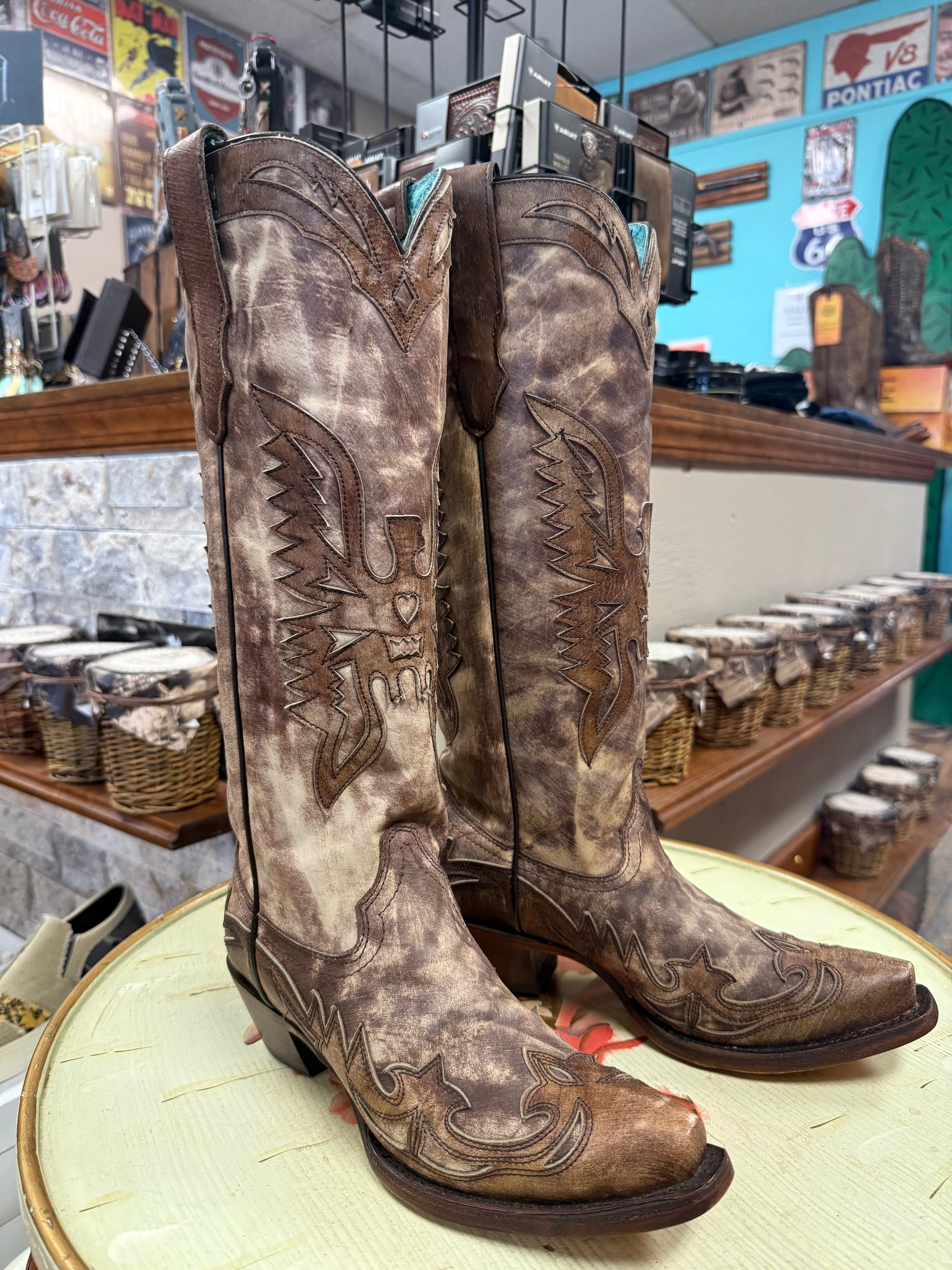 Pair of brown cowboy boots with intricate designs on a round surface in a store setting.
