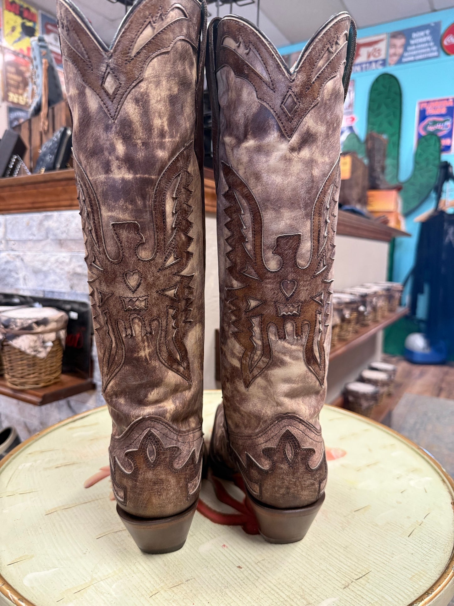 Pair of brown cowboy boots with intricate designs on a round surface.