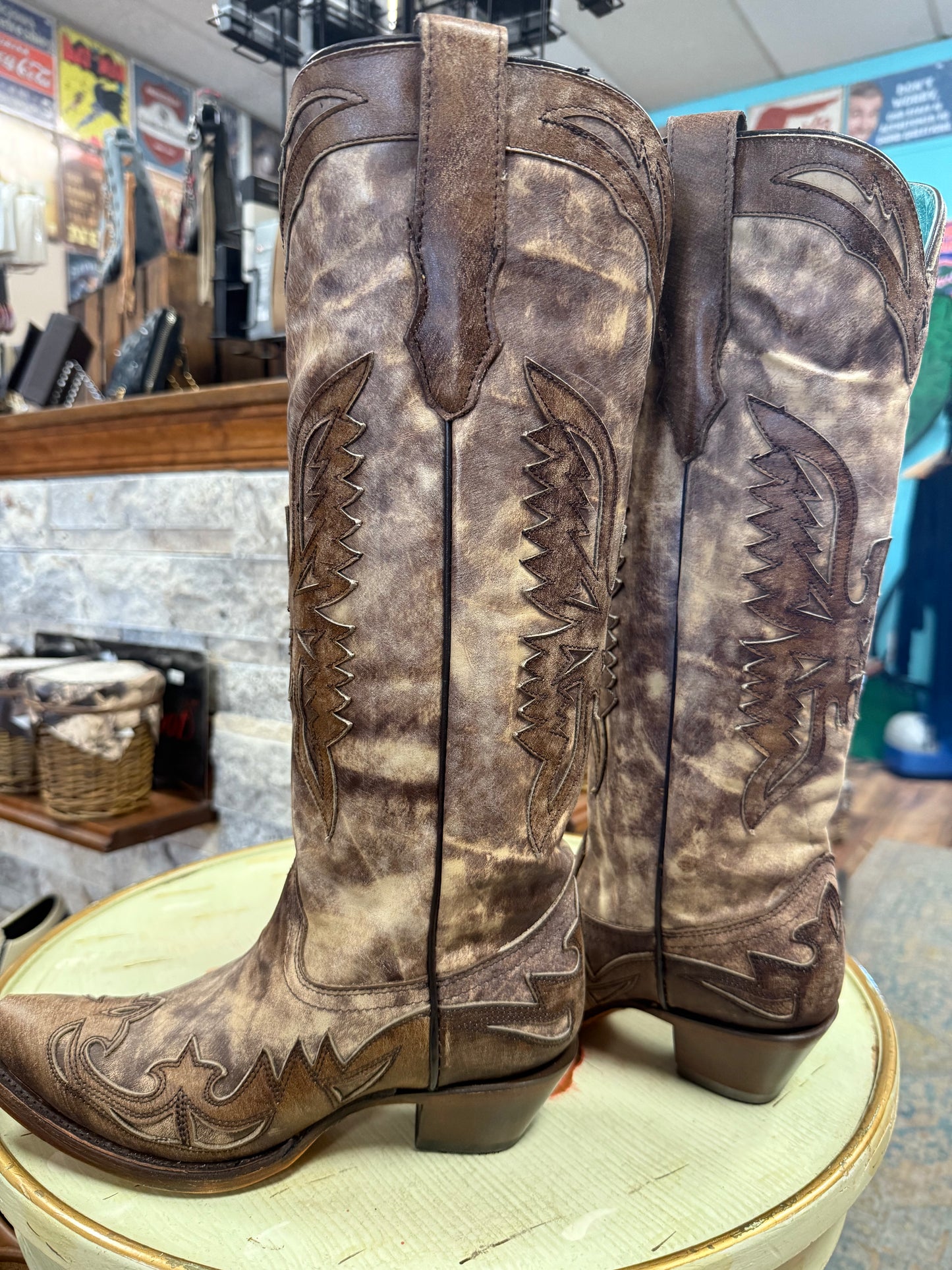 Pair of brown leather cowboy boots with intricate designs on a round surface.