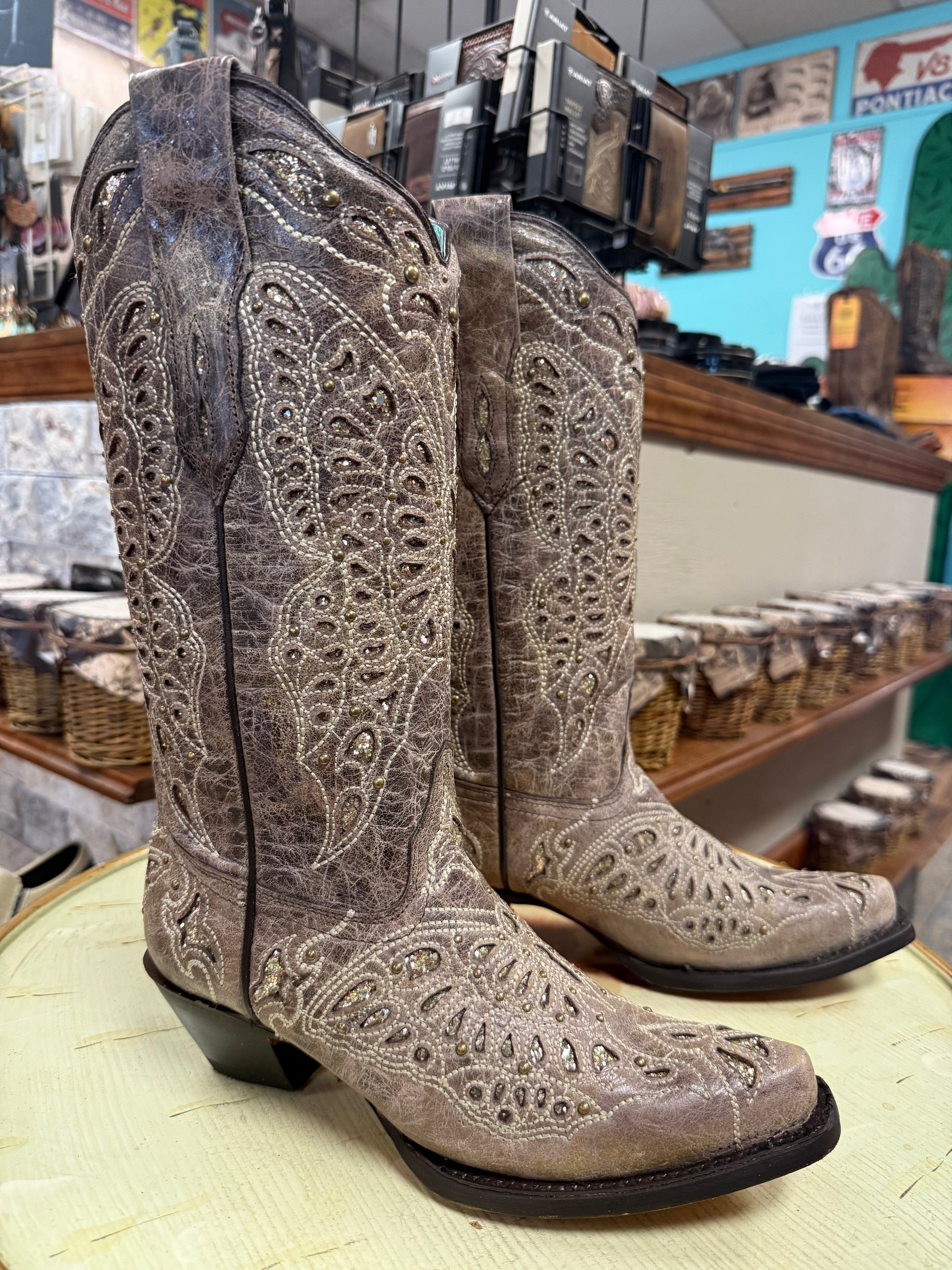 Pair of brown cowboy boots with intricate patterns on a display table.