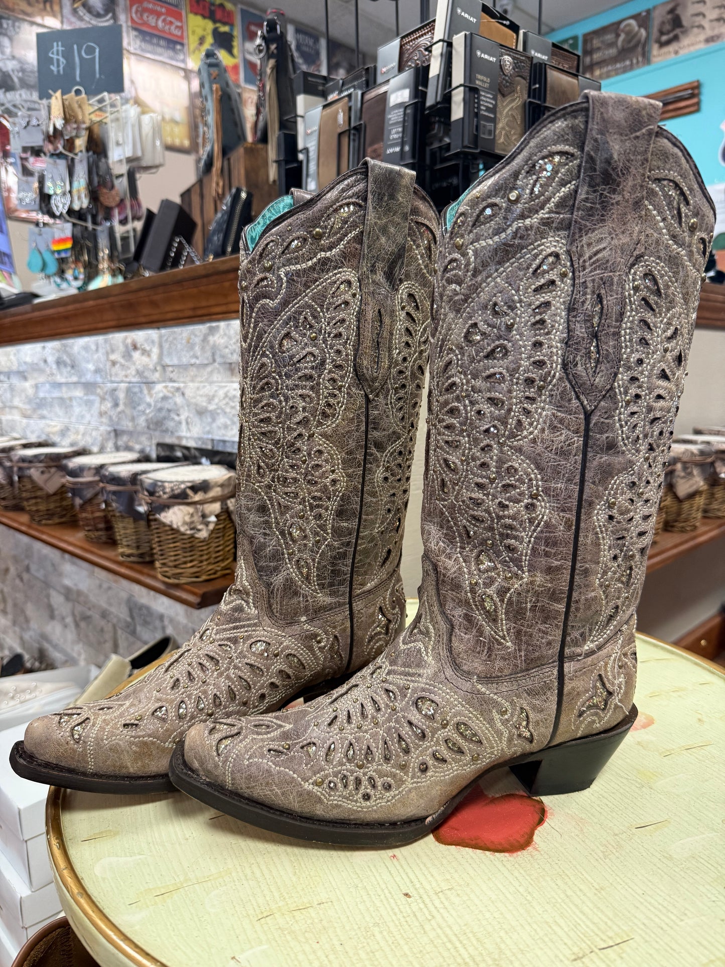 Pair of brown cowboy boots with intricate patterns on a display table in a store.