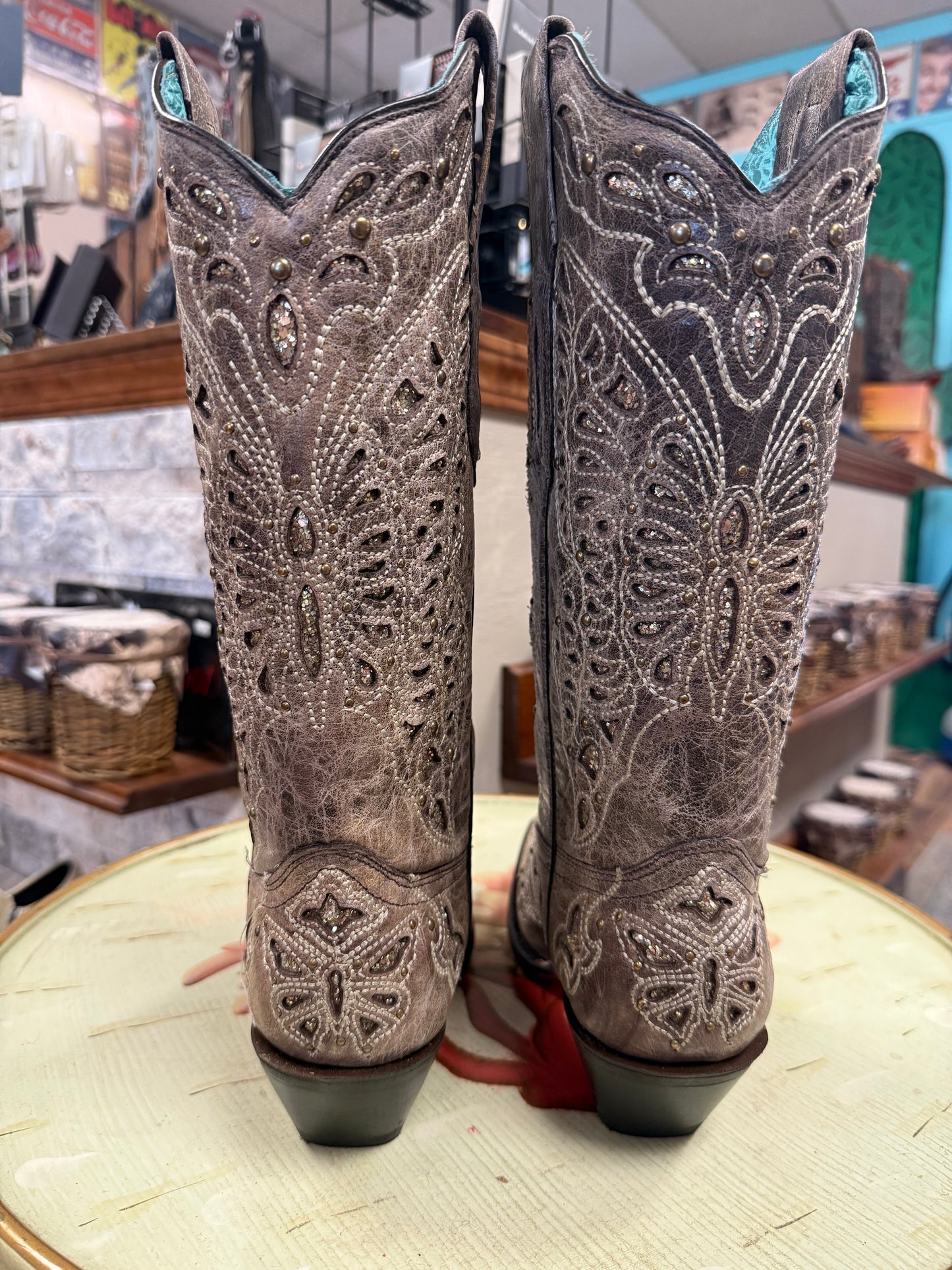 Pair of ornate cowboy boots with intricate designs on a round surface.
