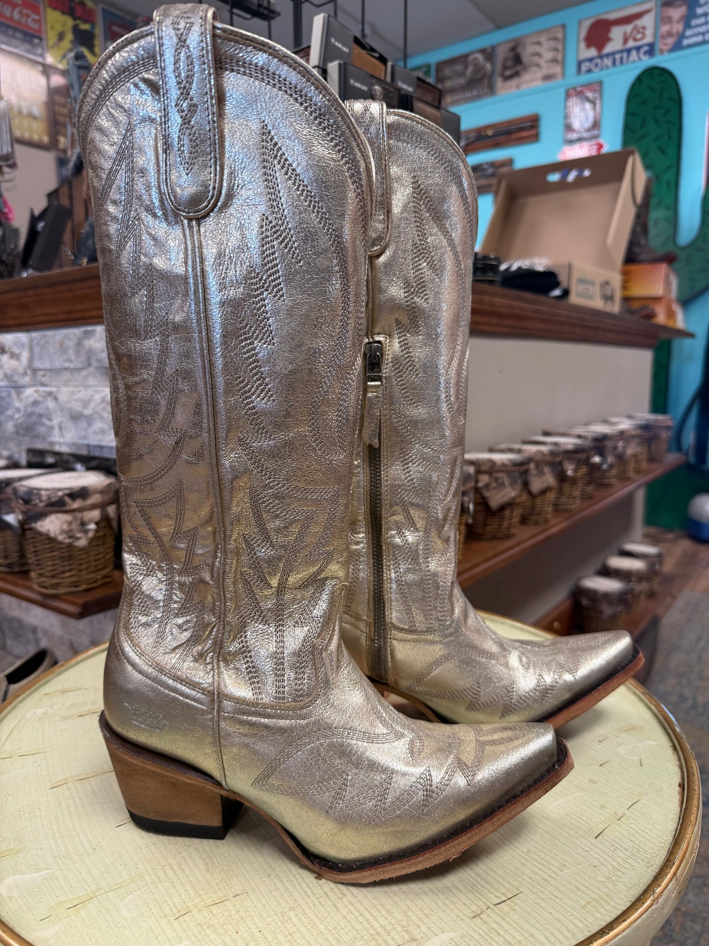 Silver cowboy boots on a round wooden surface with a store interior in the background