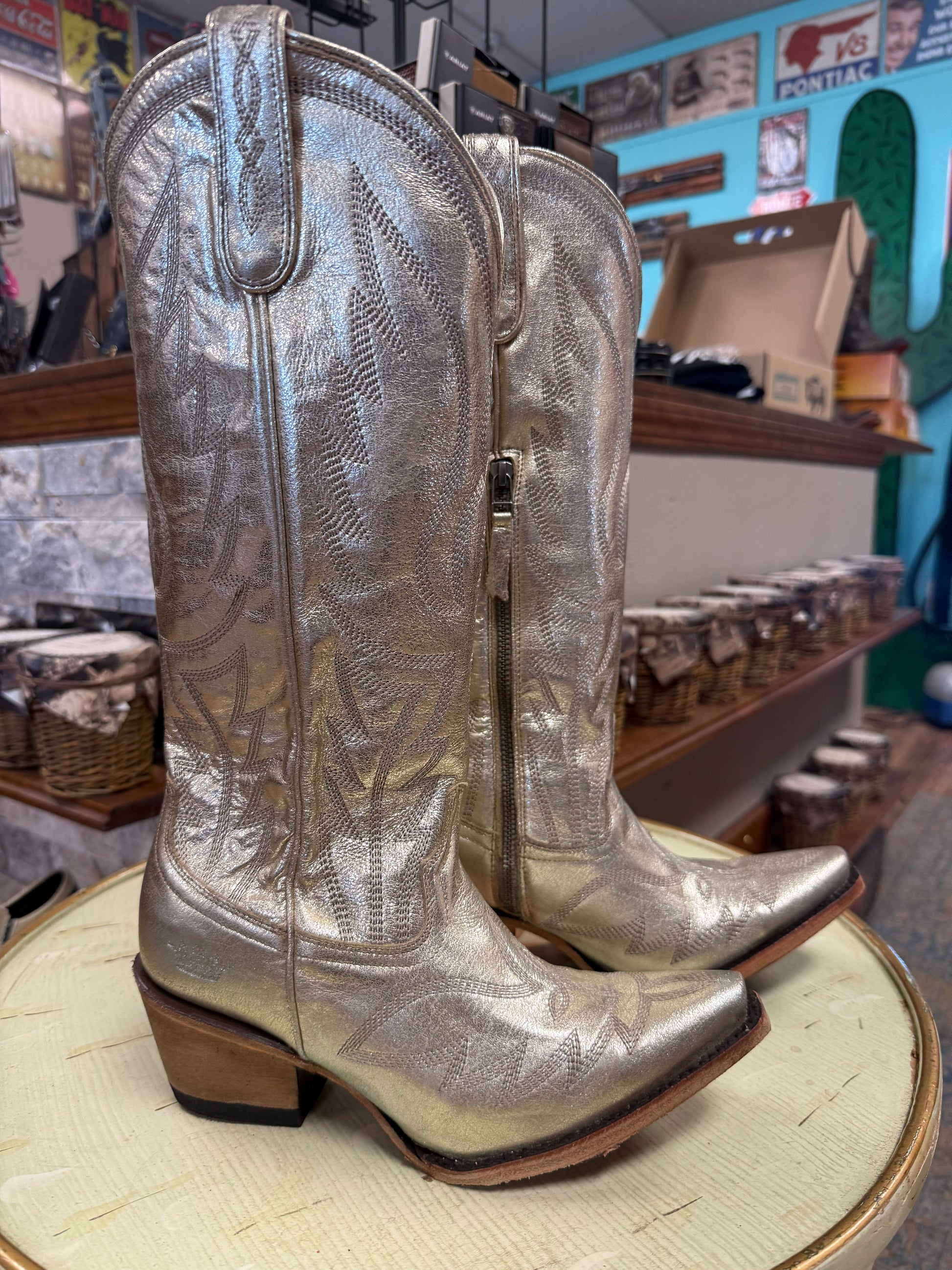 Silver cowboy boots on a round wooden surface with a store interior in the background