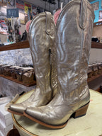 Pair of silver cowboy boots on a display stand in a store setting.