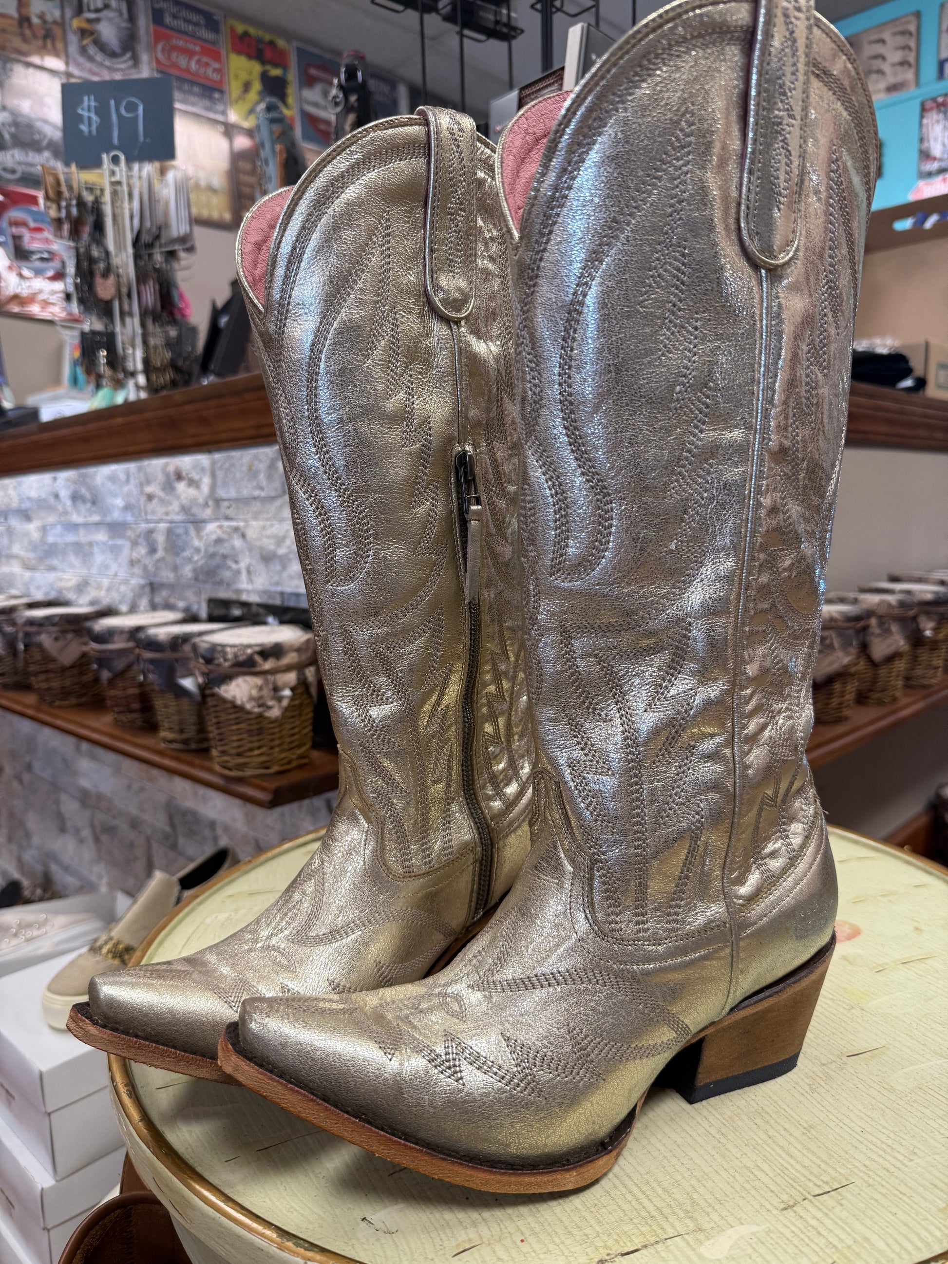 Pair of silver cowboy boots on a display stand in a store setting.