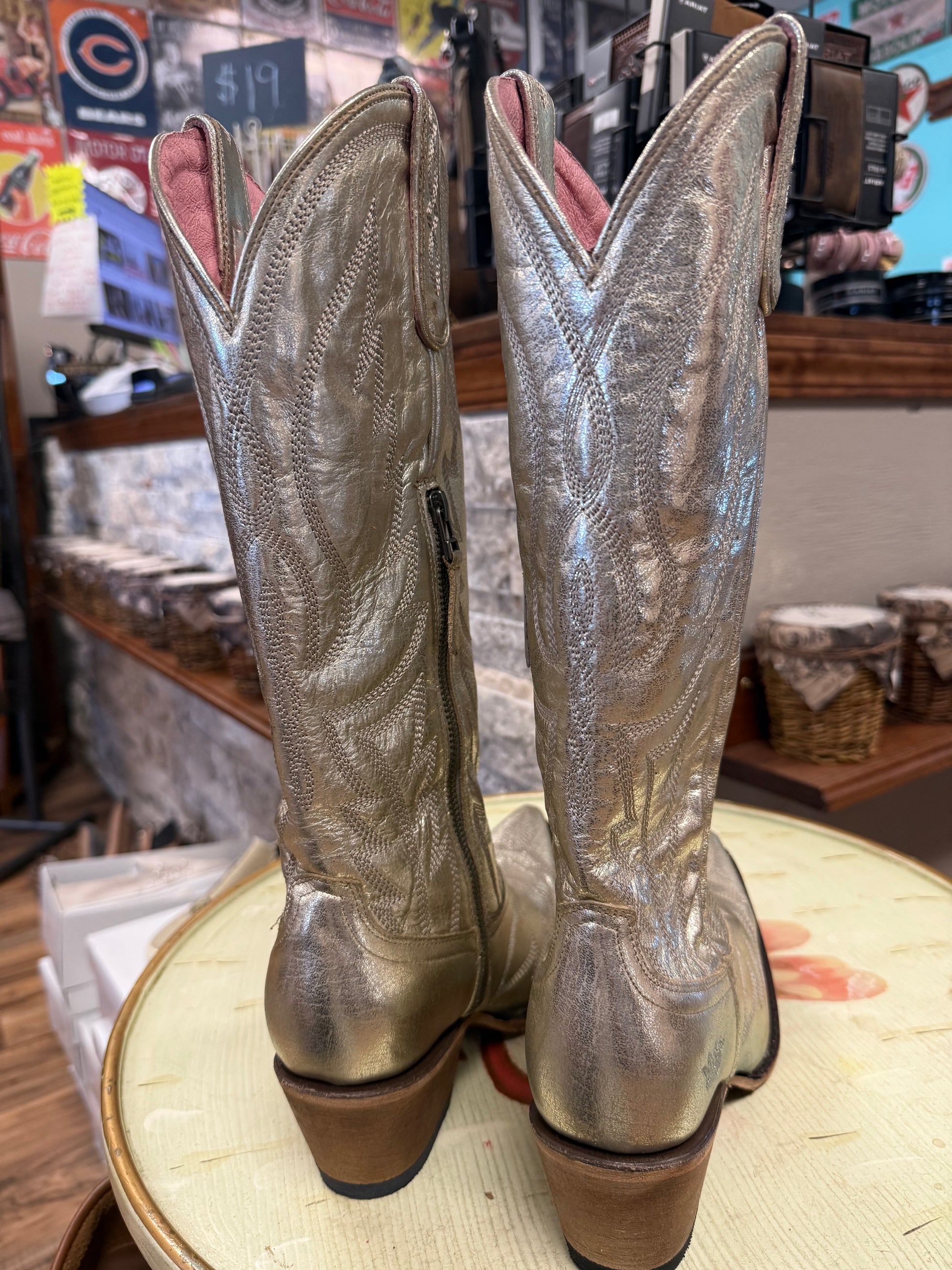 Pair of metallic gold cowboy boots on a round surface with a store interior background.