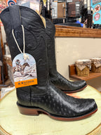 Black cowboy boots with a tag on a round surface, with a store interior in the background.
