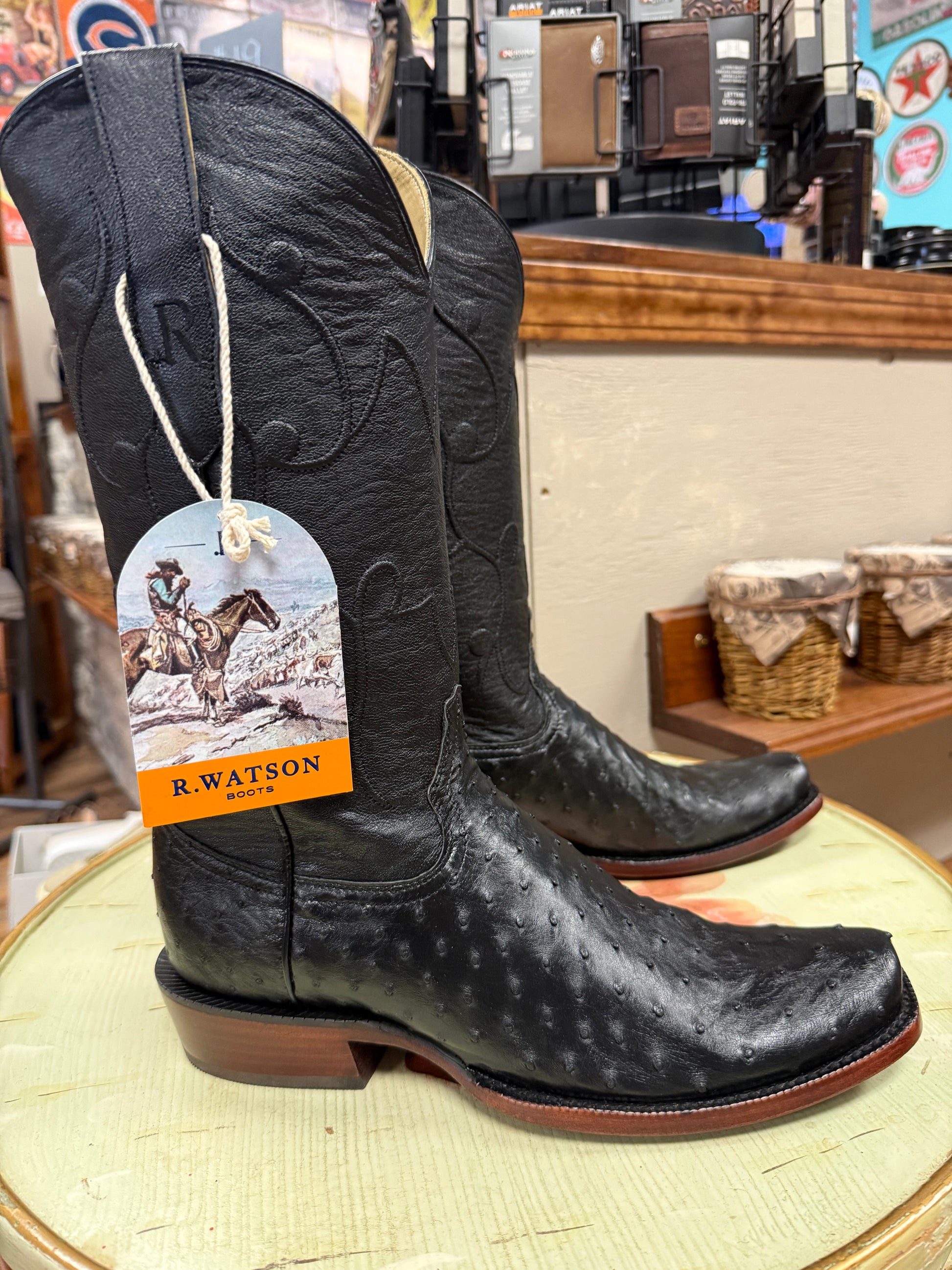 Black cowboy boots with a tag on a round surface, with a store interior in the background.