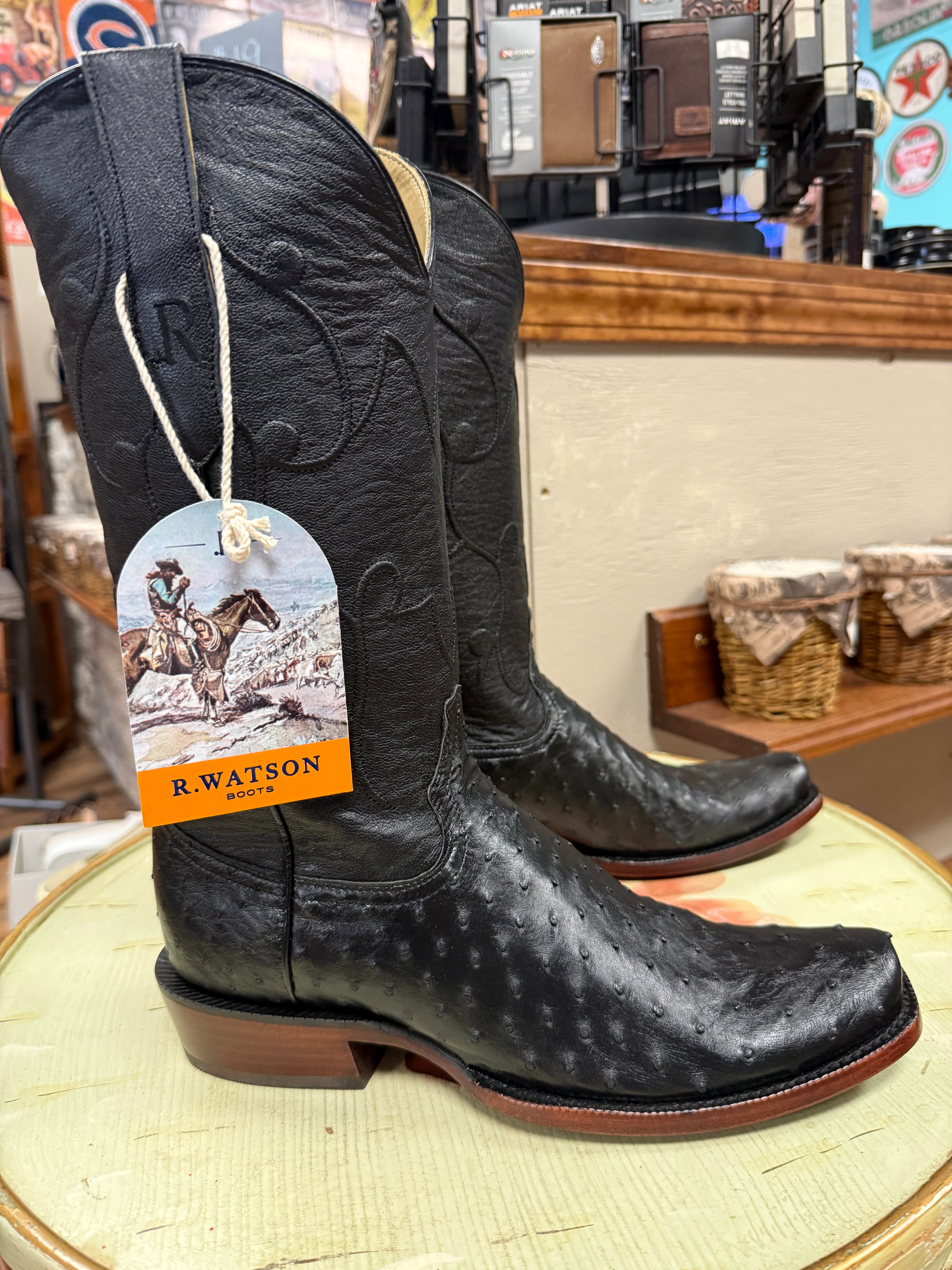Black cowboy boots with a tag on a round surface, with a store interior in the background.