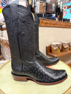 Black cowboy boots with branding on a round surface in a store setting.