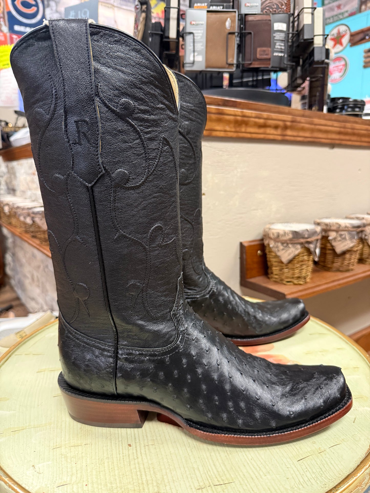 Black cowboy boots with branding on a round surface in a store setting.