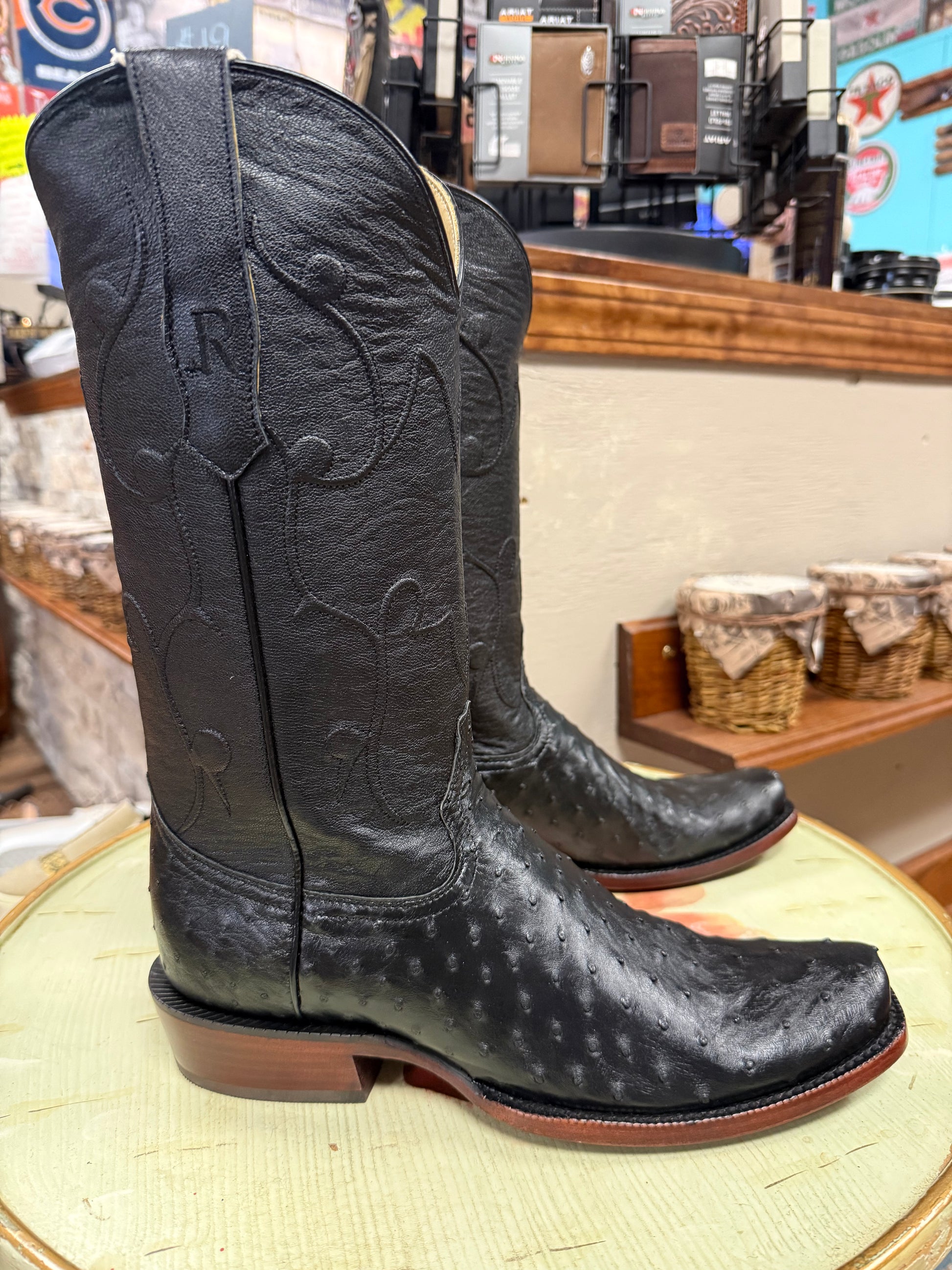 Black cowboy boots with branding on a round surface in a store setting.
