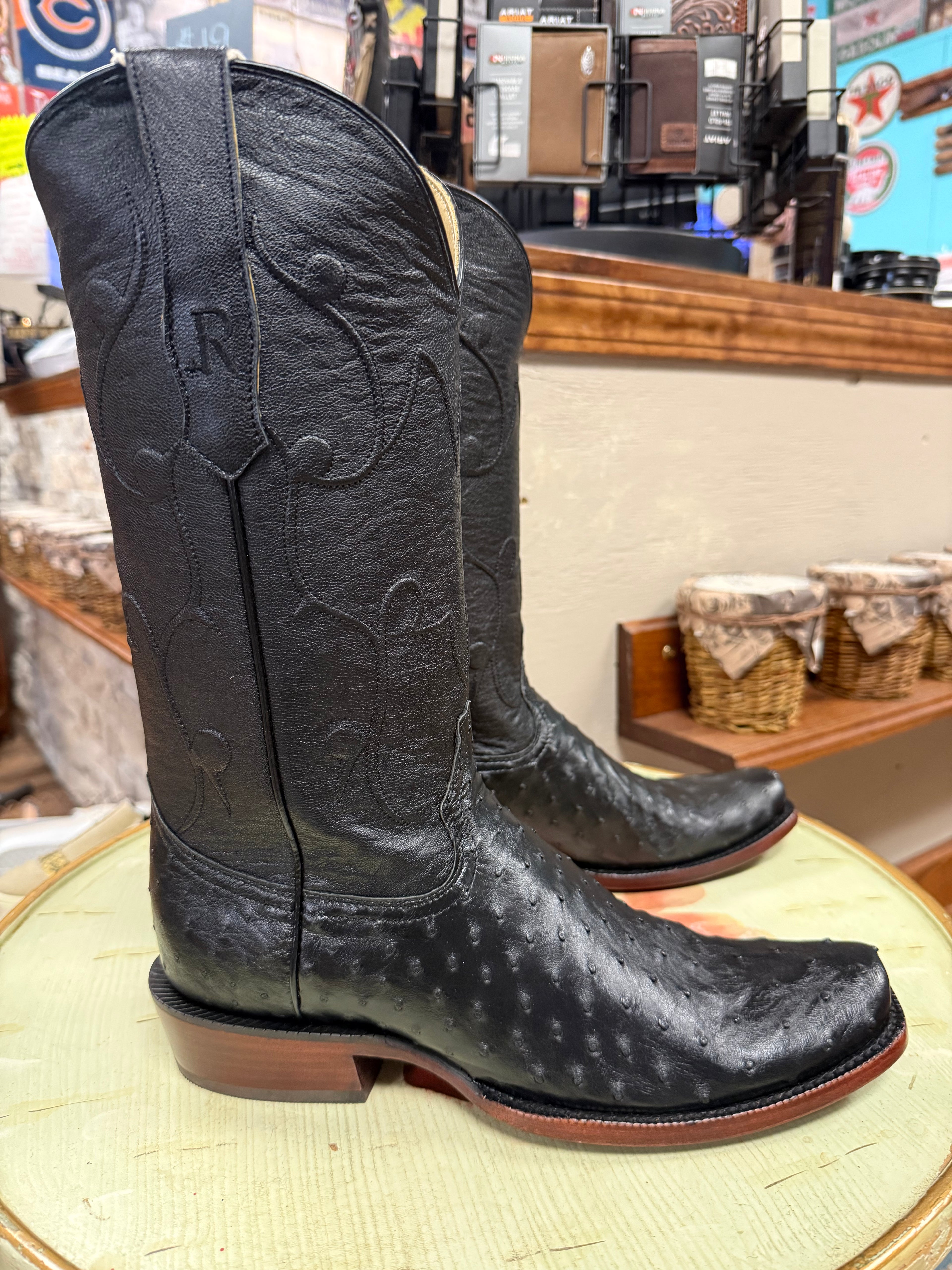 Black cowboy boots with branding on a round surface in a store setting.