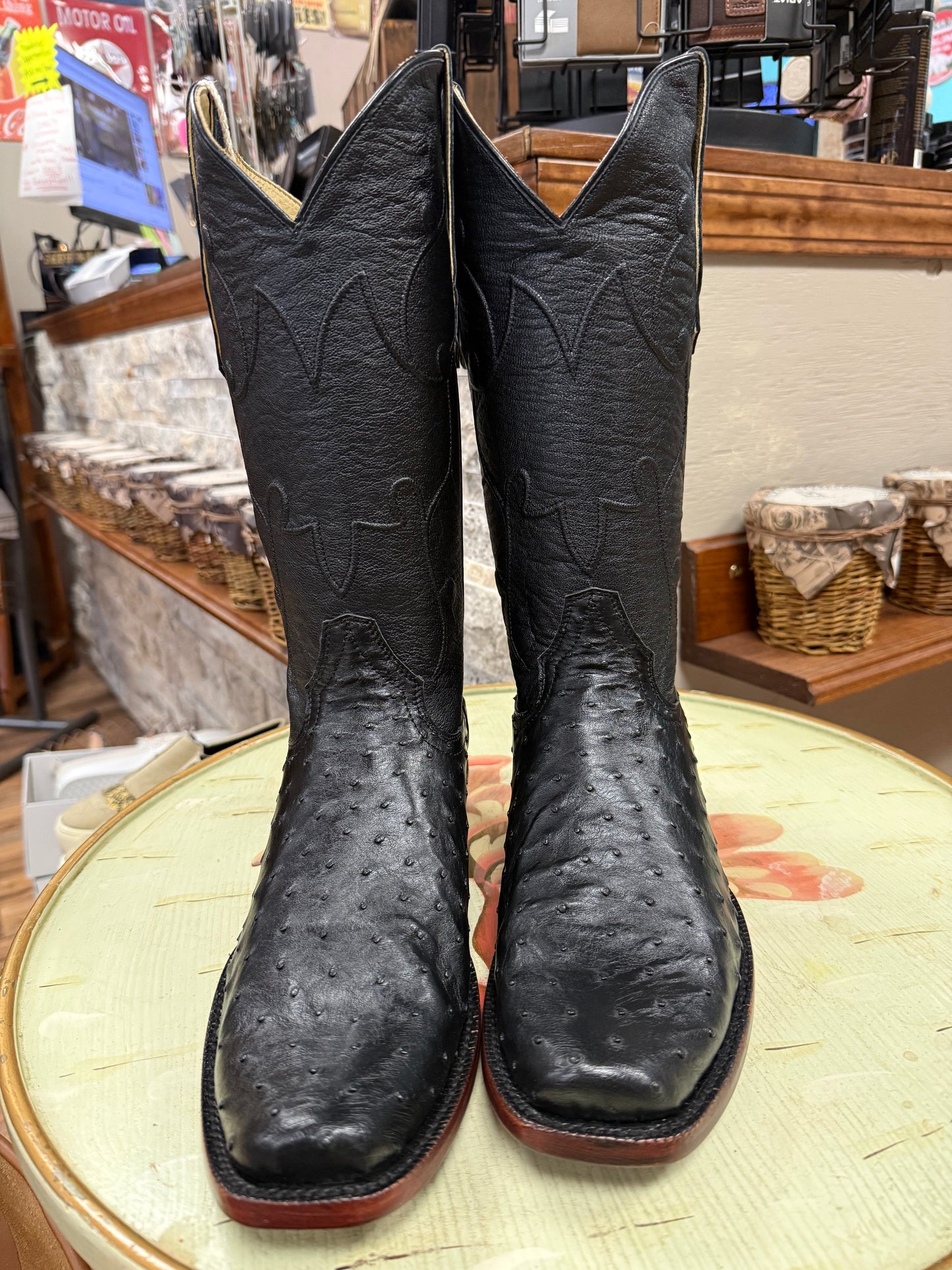 Pair of black cowboy boots on a round surface with a store interior background