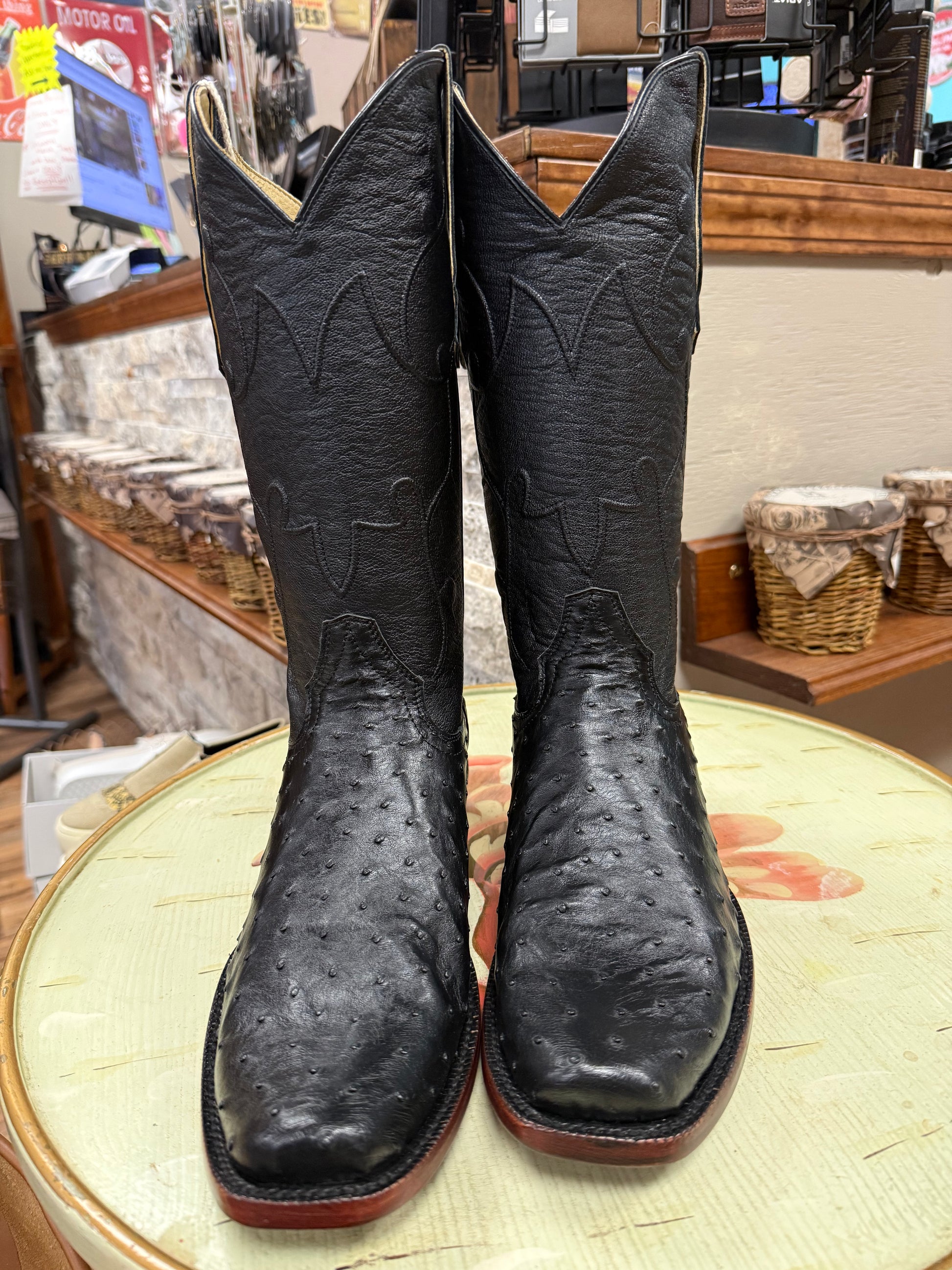 Pair of black cowboy boots on a round surface with a store interior background