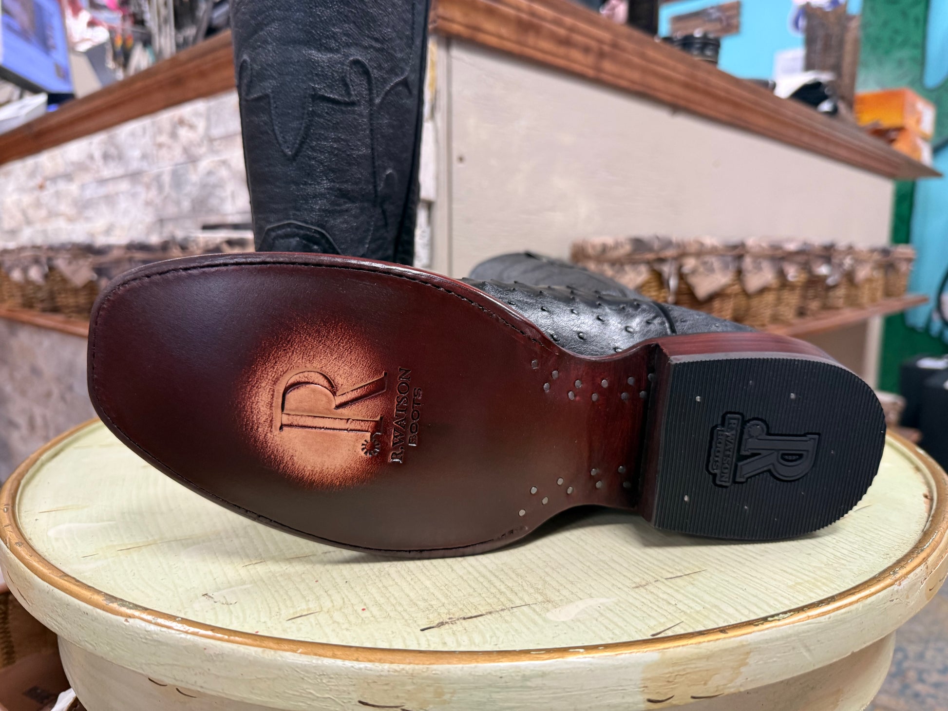 Close-up of a brown leather shoe sole with a brand logo on a light green surface.