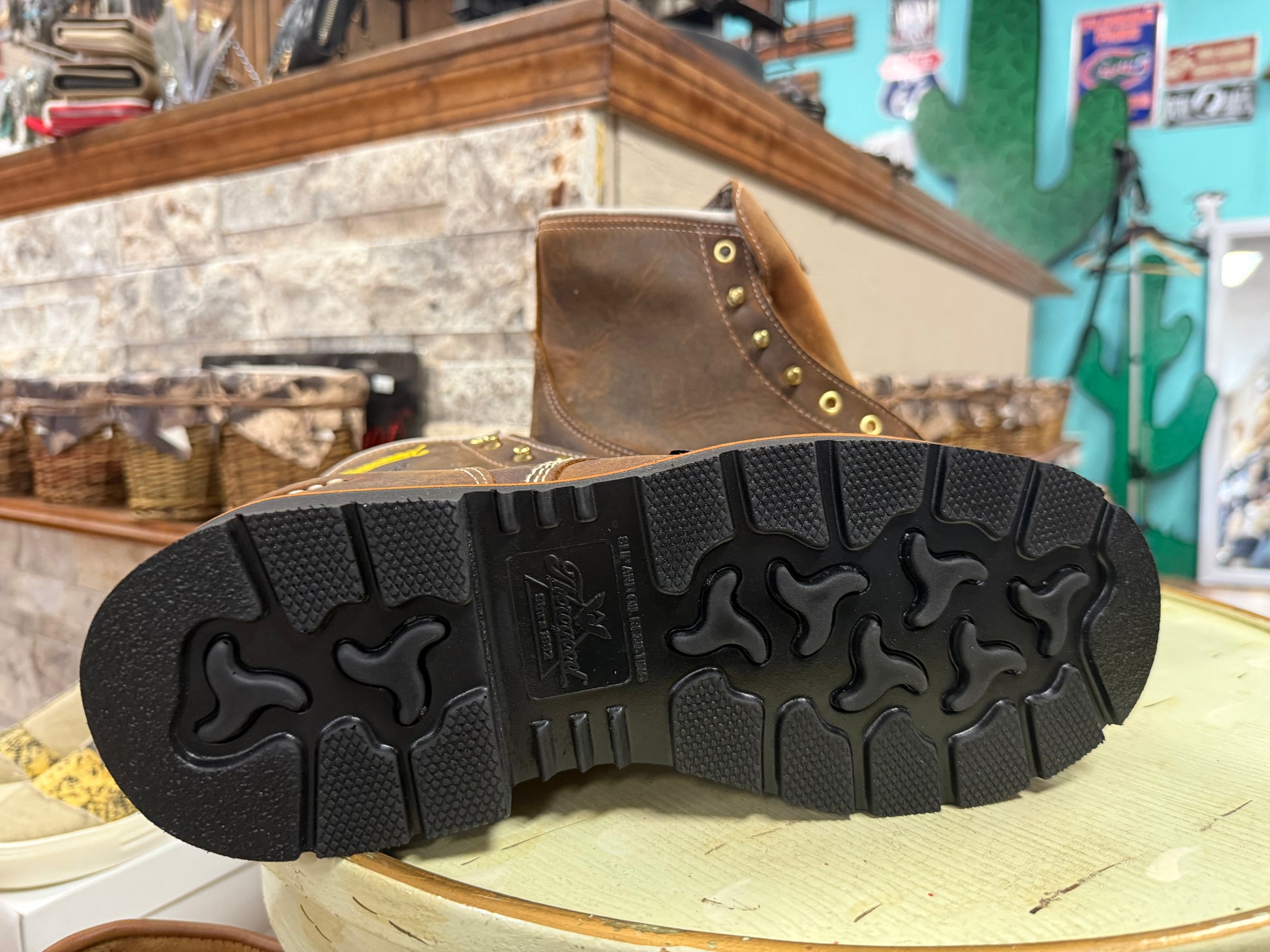 Brown leather boot with black sole on a wooden surface, store interior in the background