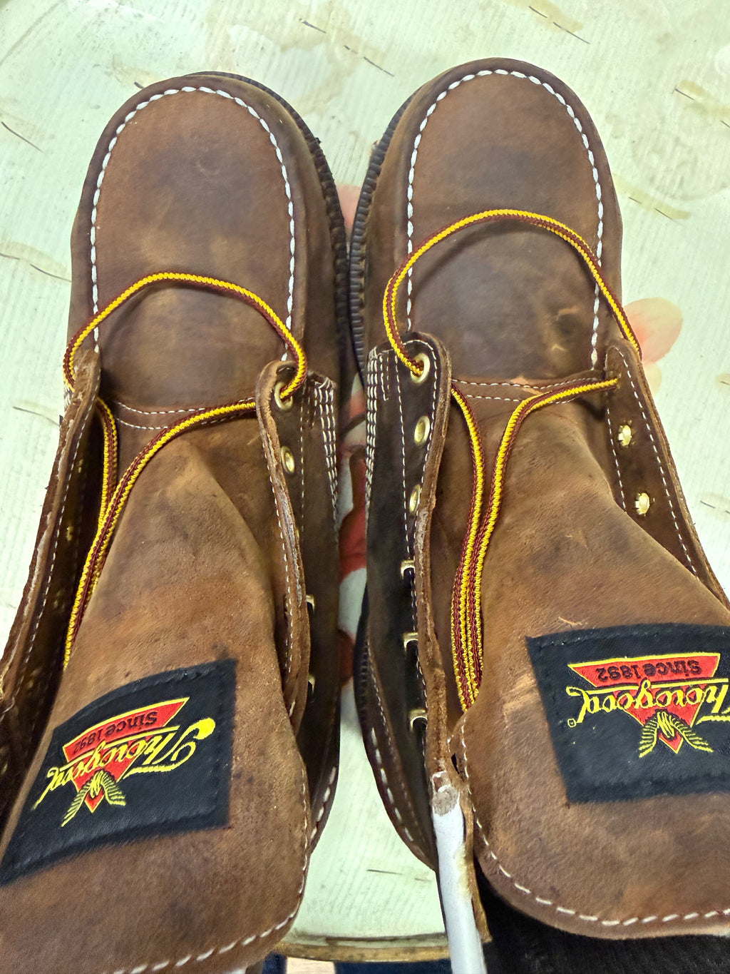 Pair of brown leather shoes with yellow stitching on a light background