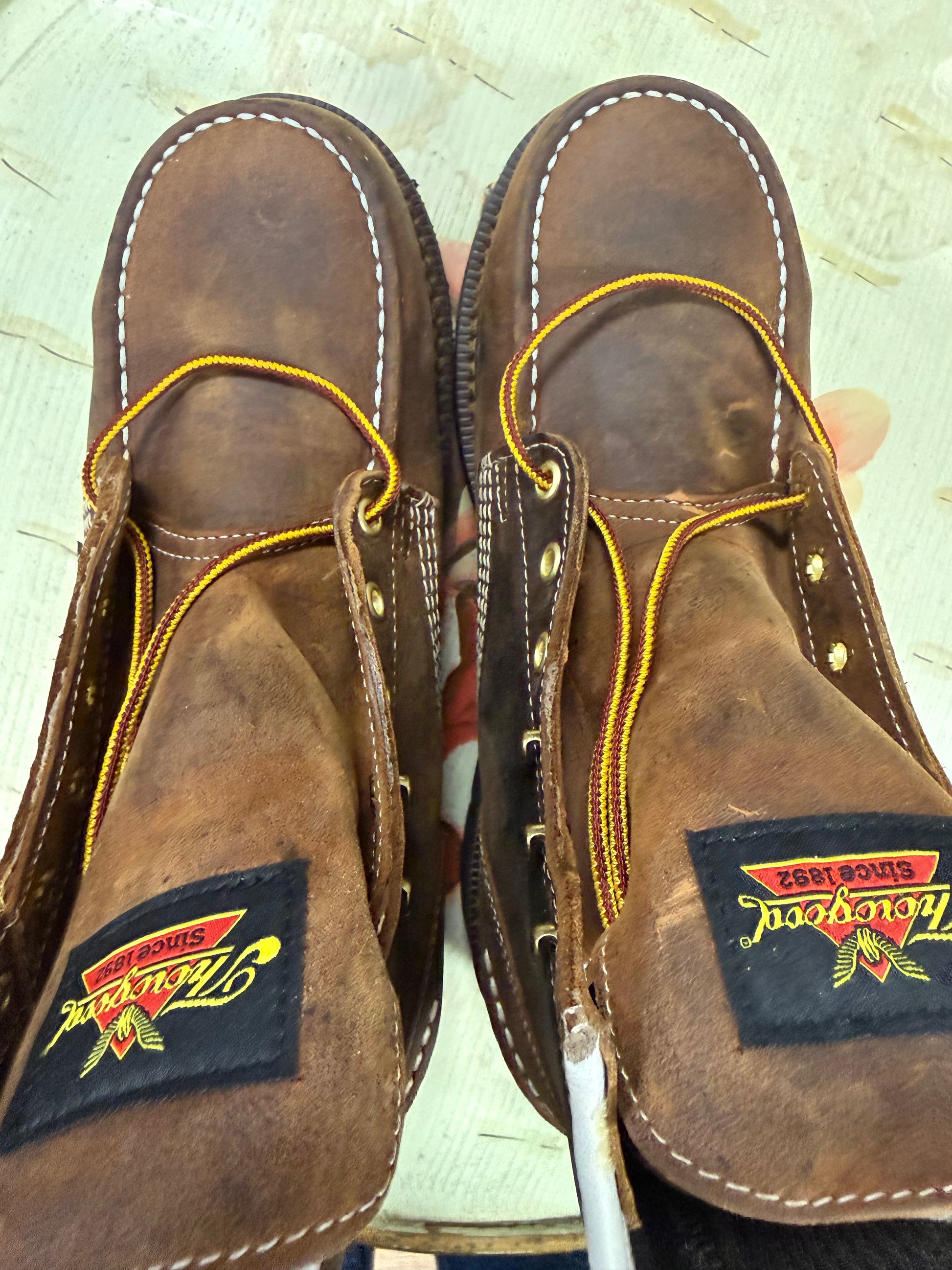 Pair of brown leather shoes with yellow stitching on a light background