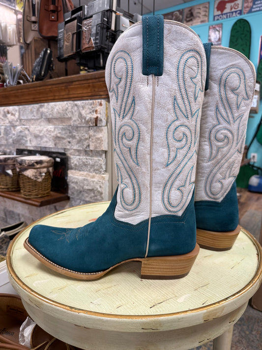 Pair of blue and white cowboy boots on a round wooden stool in a store setting.