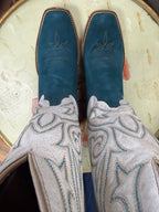 Pair of blue cowboy boots with intricate white and blue embroidery on a textured surface.
