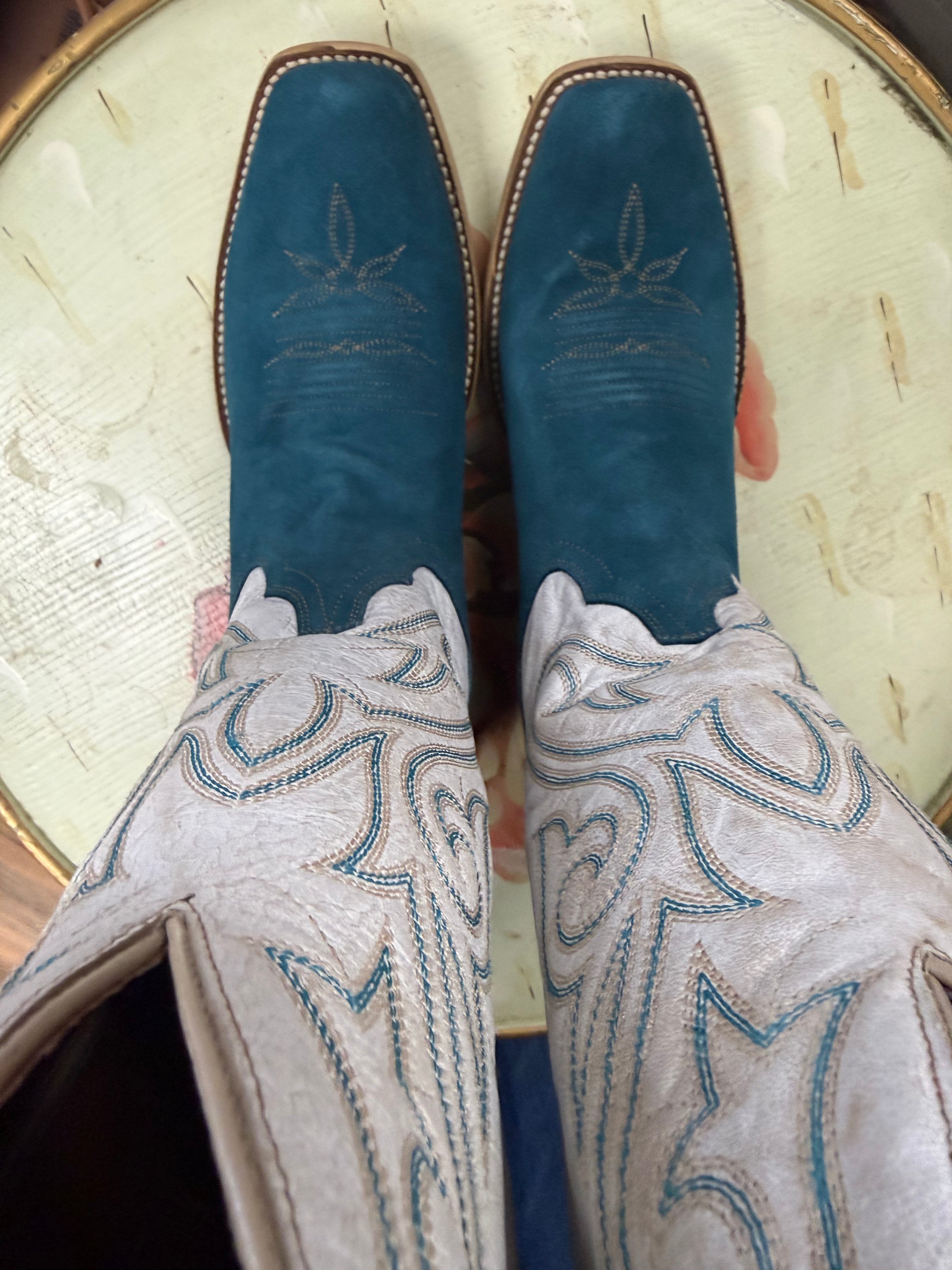 Pair of blue cowboy boots with intricate white and blue embroidery on a textured surface.