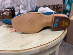 Close-up of a blue cowboy boot with a visible brand logo on the sole, placed on a worn wooden stool.