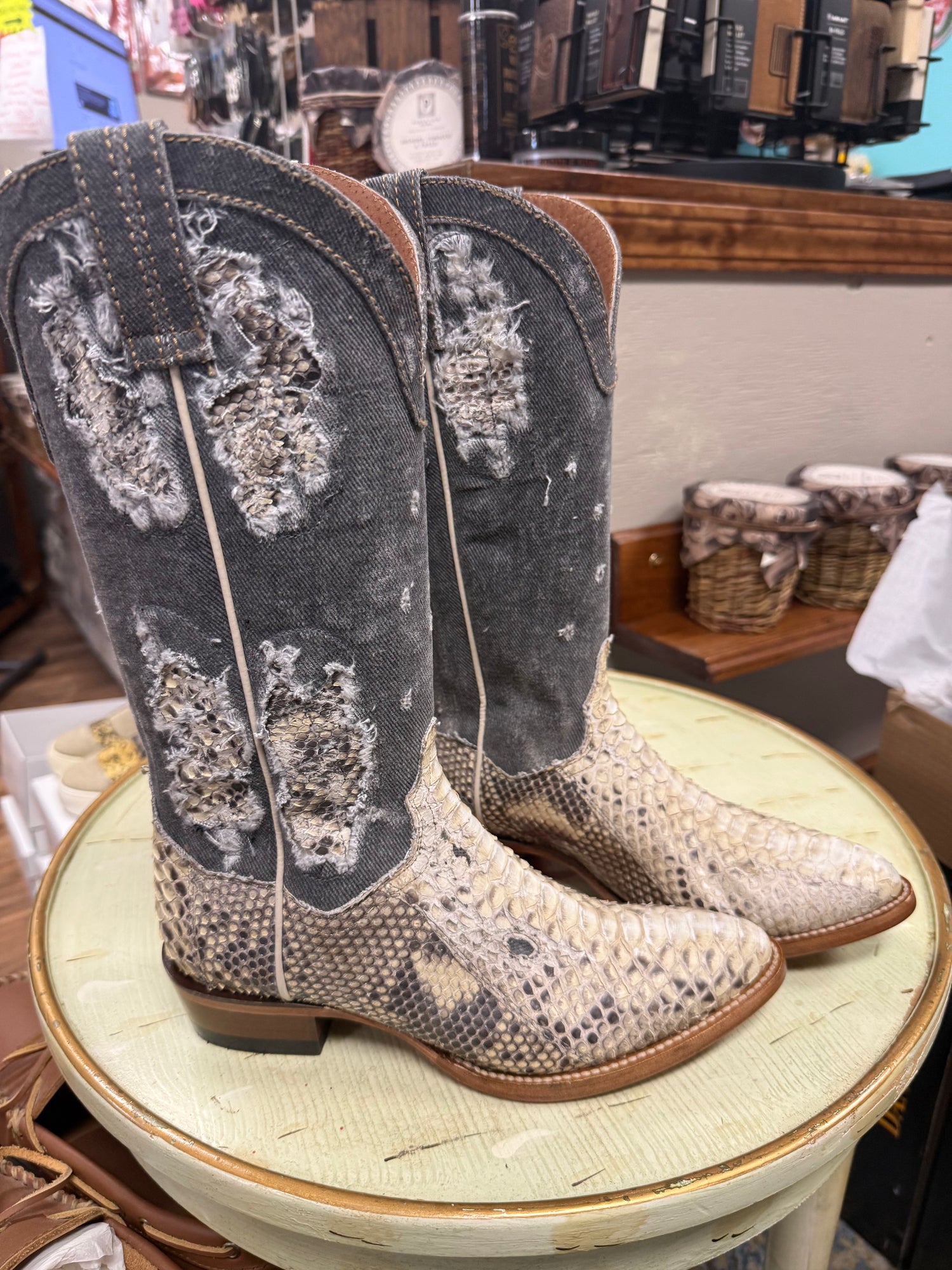 Pair of cowboy boots with snake print on a stool in a store setting