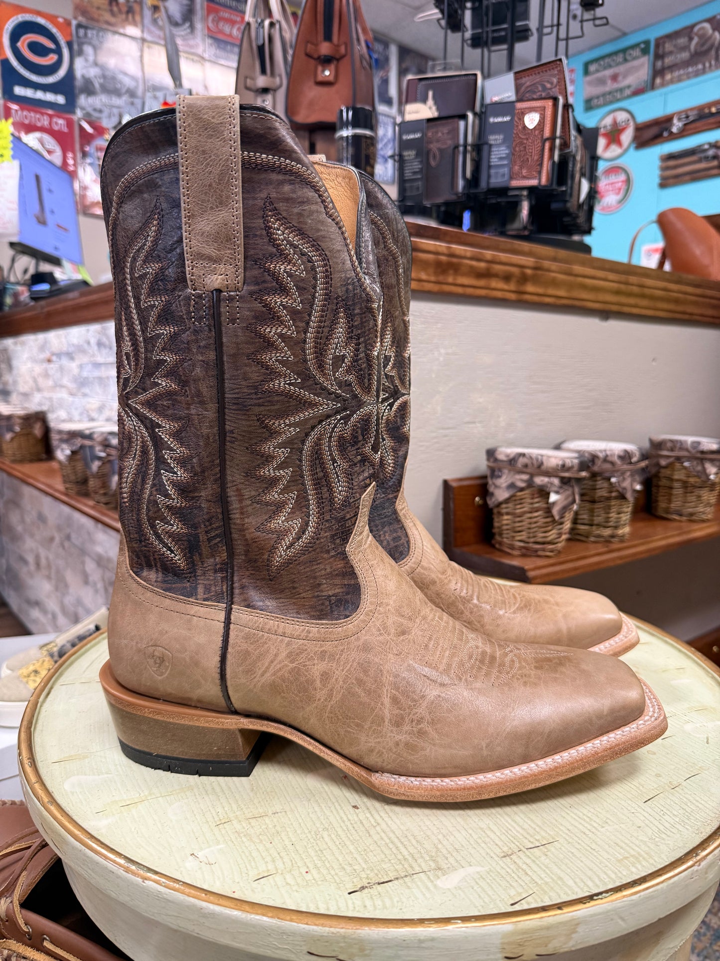 Pair of brown and beige cowboy boots on a wooden stand in a store setting.