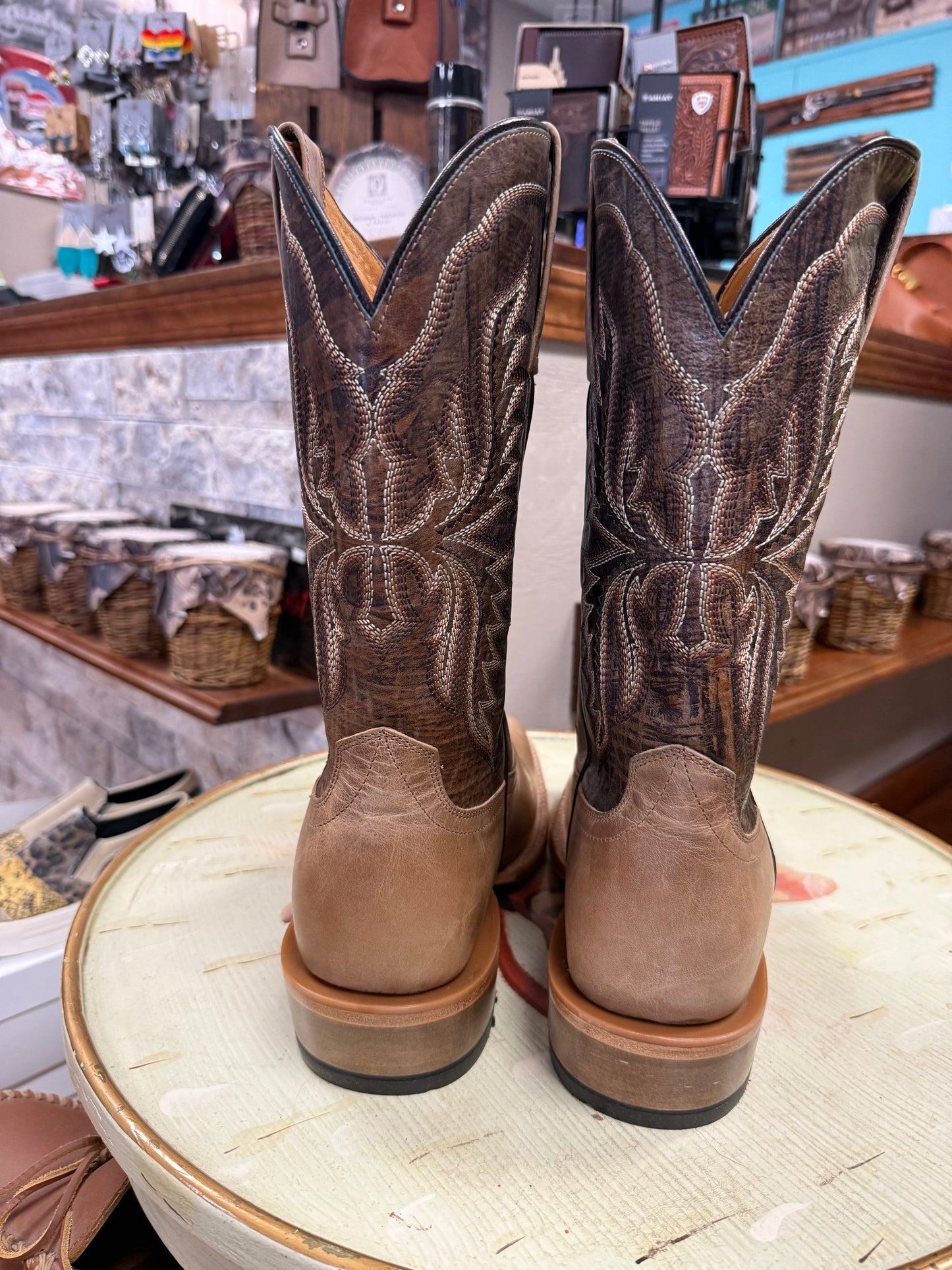 Pair of brown cowboy boots on a table with a store interior in the background